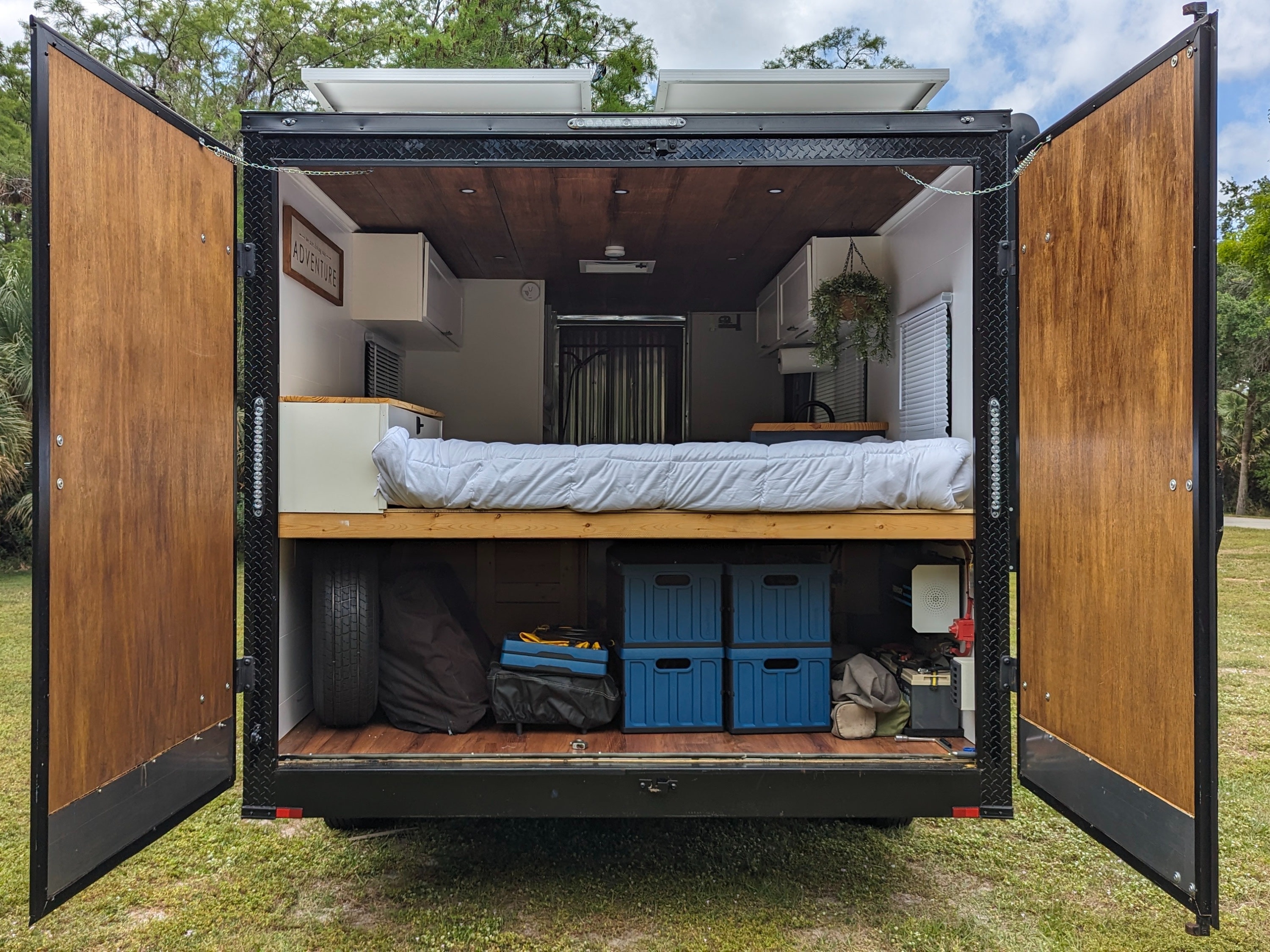 Converted cargo trailer rv rental with rear doors open, revealing a cozy bed, ample storage, and solar panels.. Diamond Cargo 16x8.5 2023