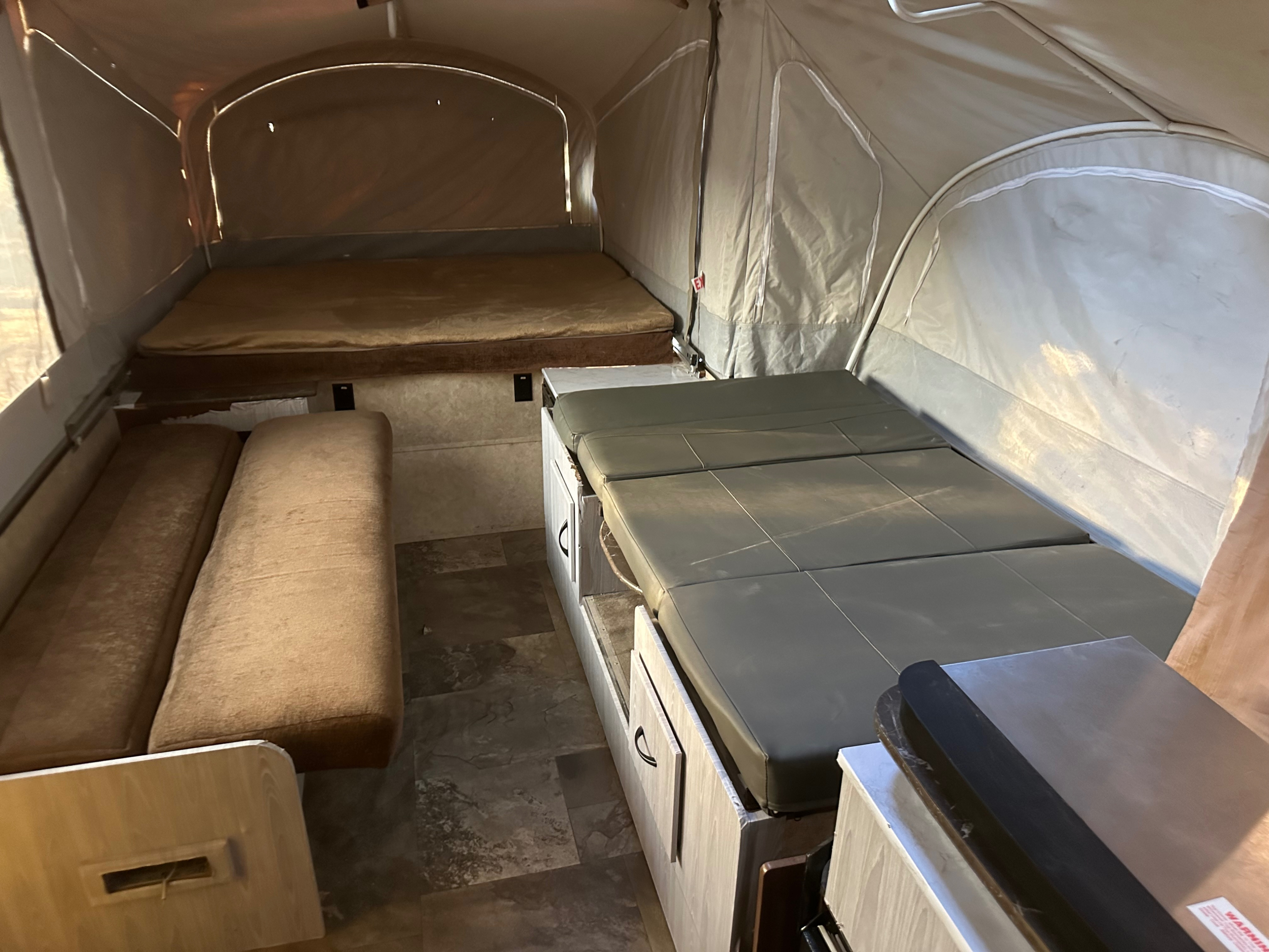 Interior of an RV rental pop-up camper, featuring two beds, a bench seat, and a compact kitchenette.. Jayco 1209SC 2016