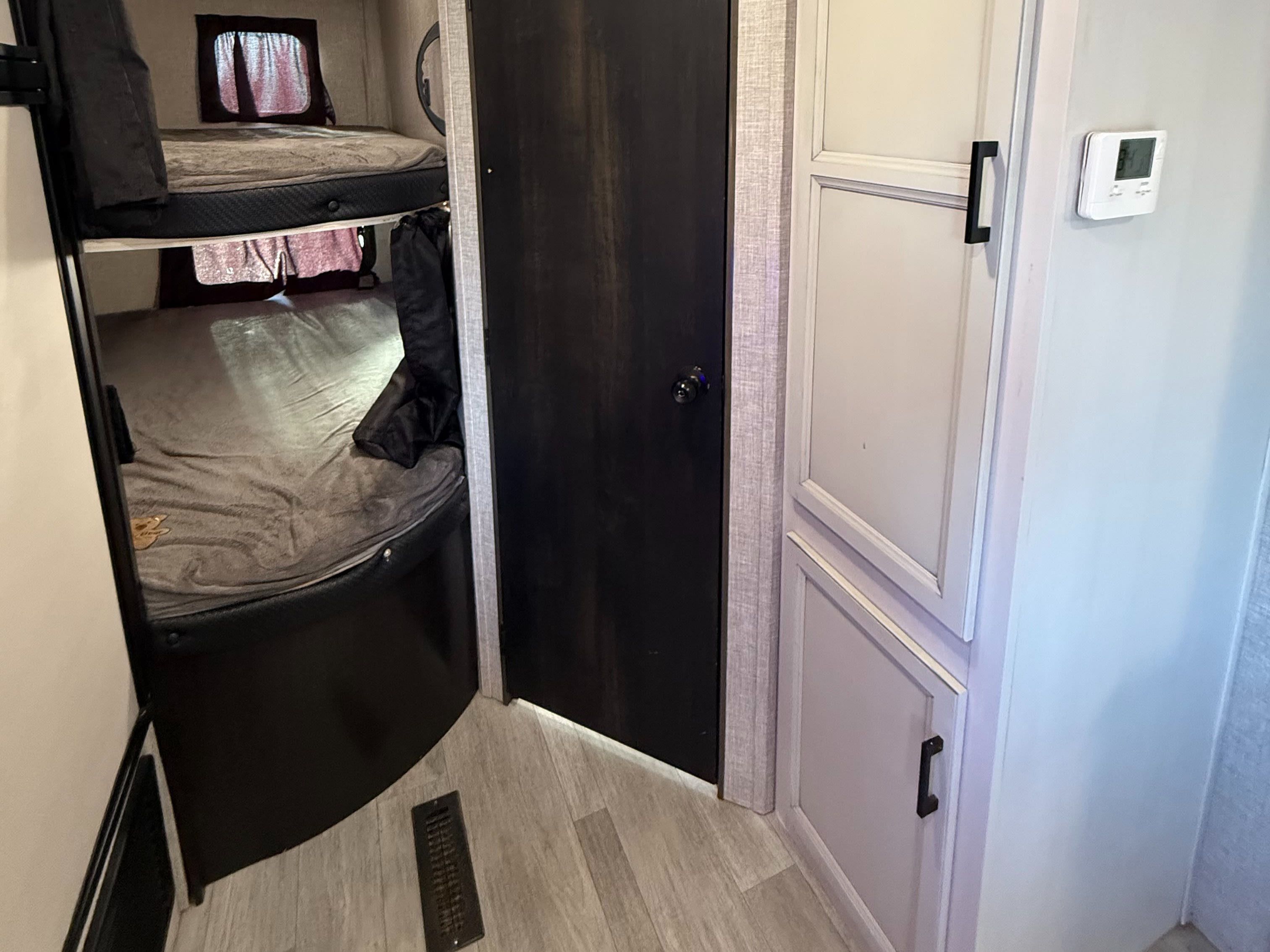 An rv rental interior: bunk beds on left, dark door, light cabinets with a wall thermostat on the right.. Jayco Jay Flight SLX Rocky Mountain Edition 2022