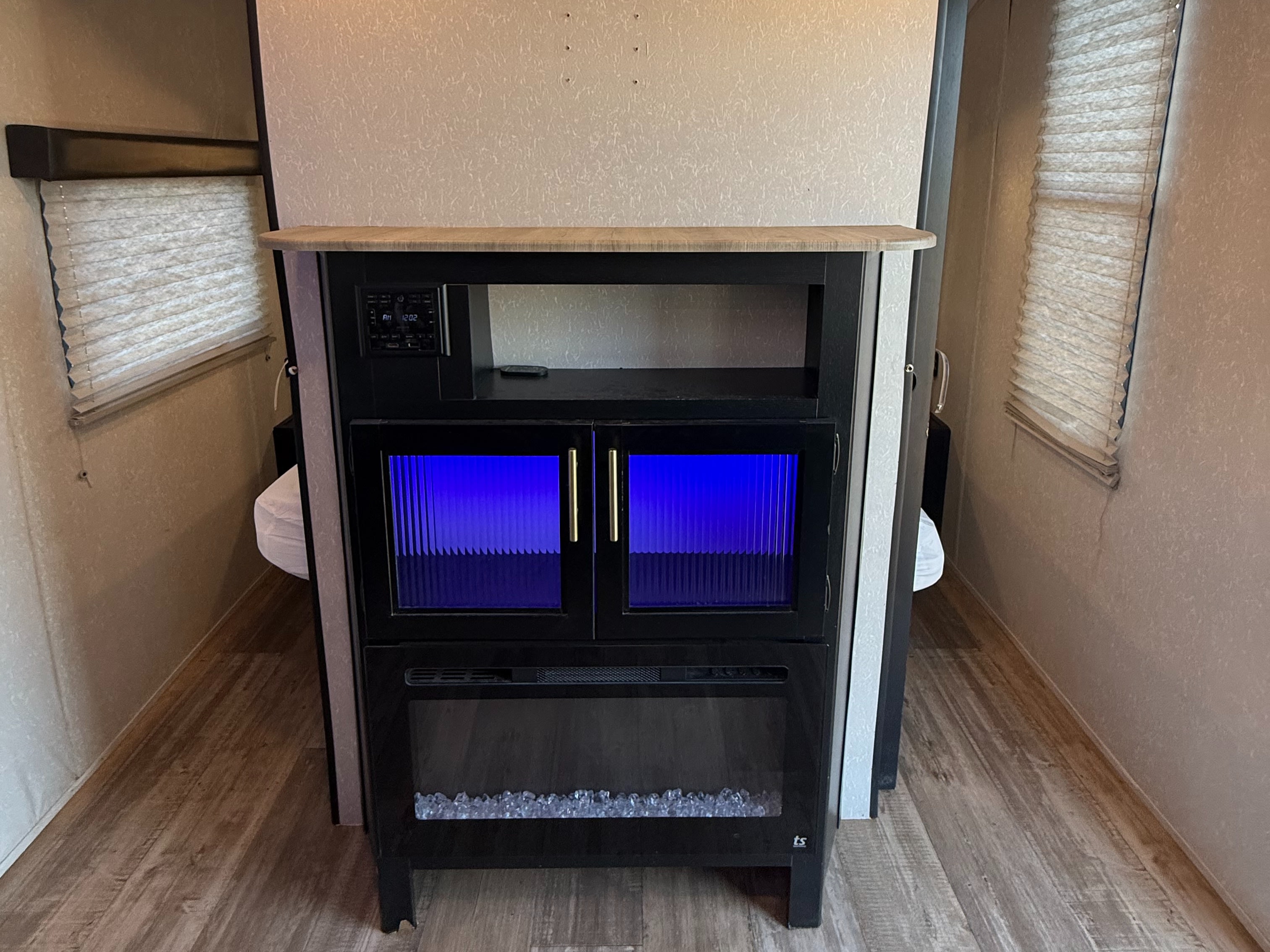 RV rental living area: black entertainment center with blue-lit cabinets, a stereo, and an electric fireplace between two windows.. Forest River Cherokee Grey Wolf 2021