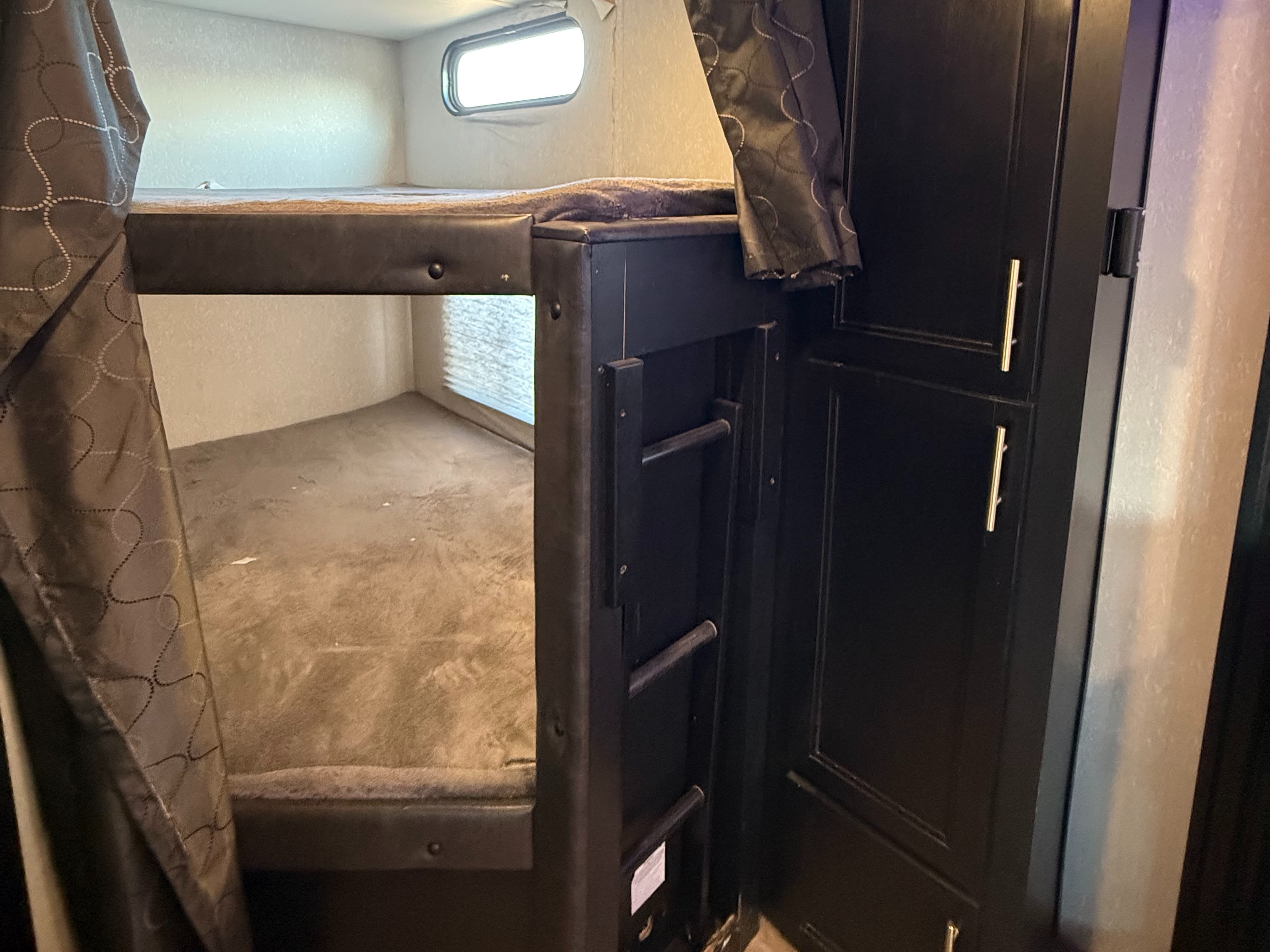 Inside an RV rental: a bunk bed sleeping area with a small ladder, window, and cabinet storage.. Forest River Cherokee Grey Wolf 2021
