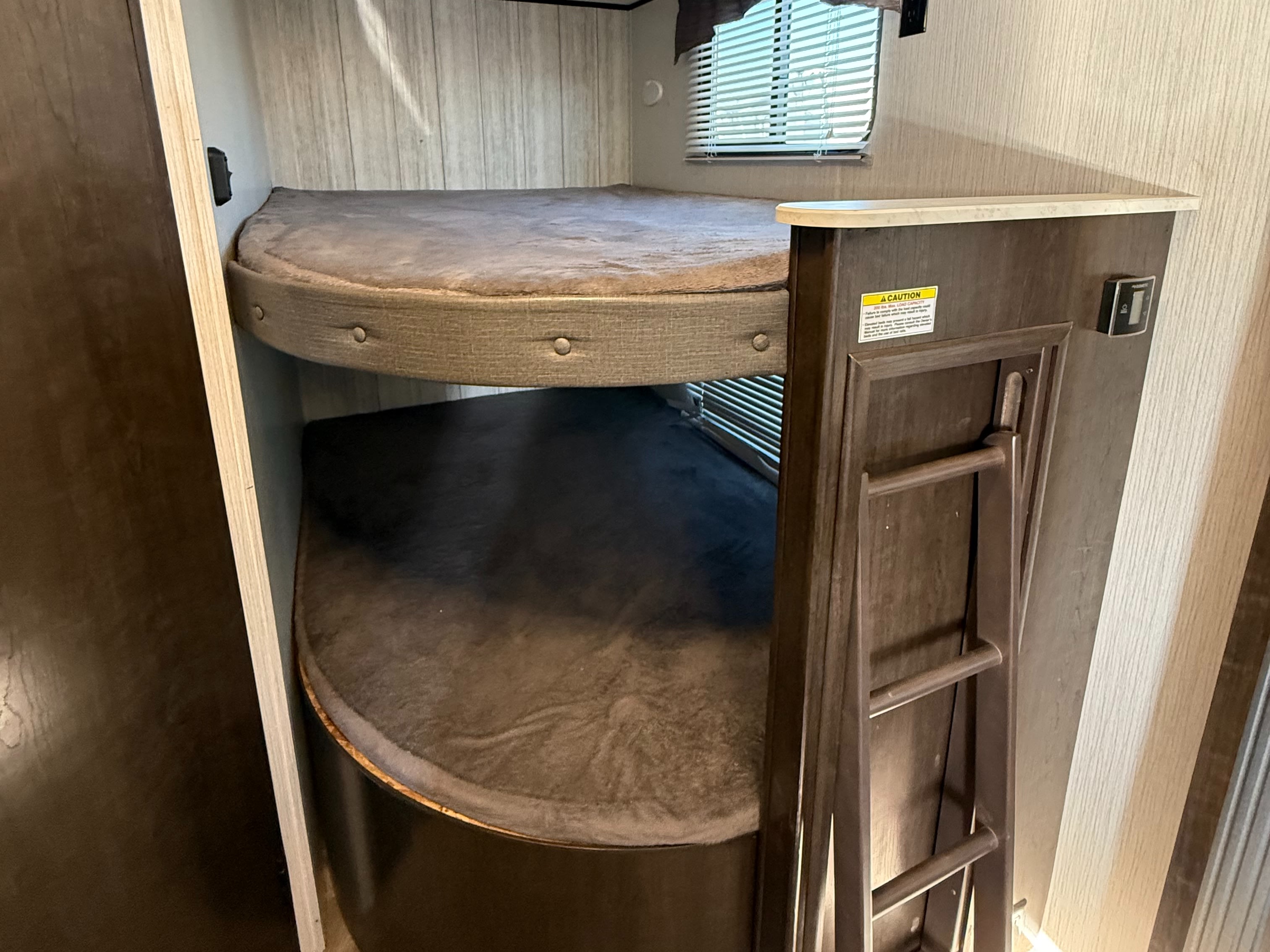 RV rental featuring stacked bunk beds with cushions and a side ladder. A window with blinds is visible above the top bunk.. Heartland RVs Pioneer 2021