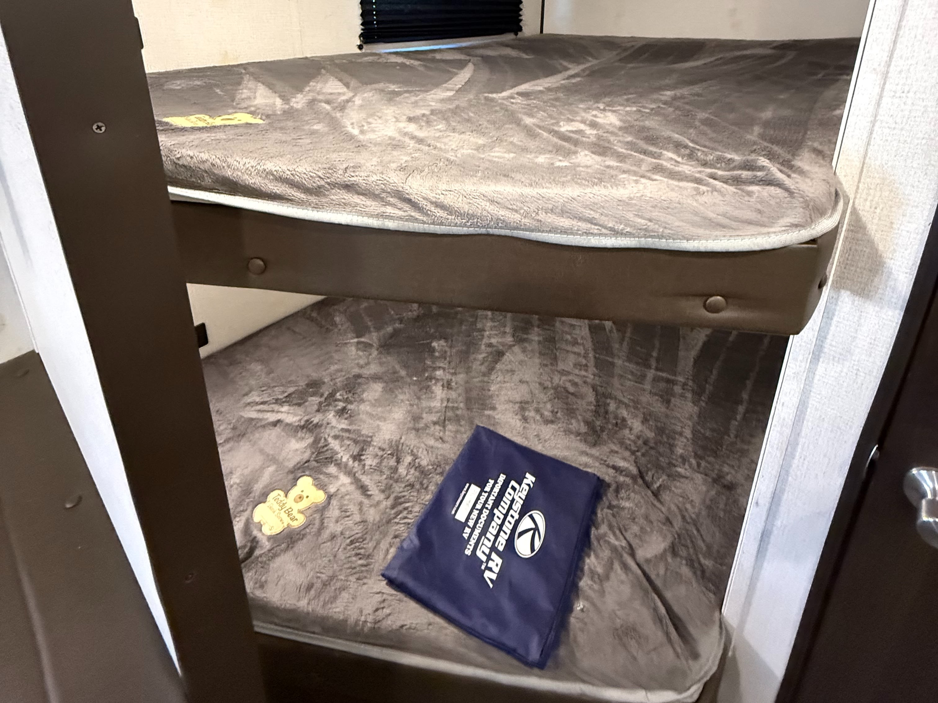 Cozy bunk beds in an RV rental, featuring Keystone RV documents and a cute "Teddy Bear" tag on the lower bunk. Perfect for family camping.. Keystone RV Springdale 2021