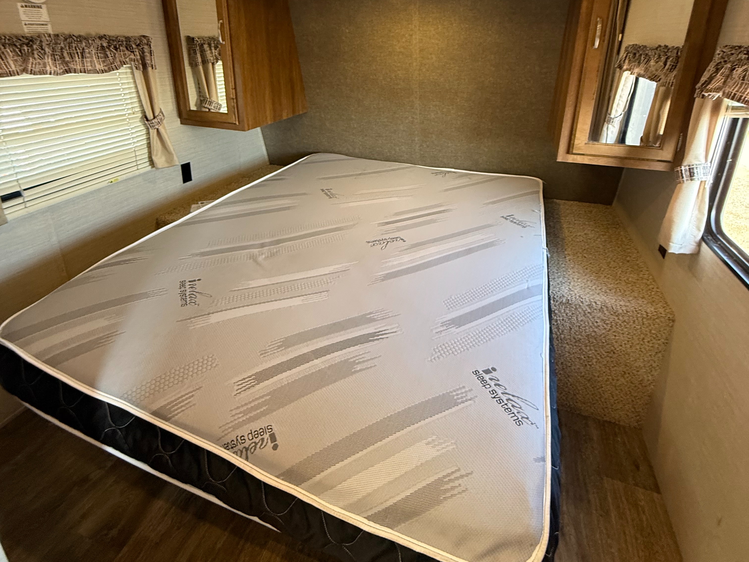 This RV rental bedroom features an iRelax Sleep Systems mattress, window with blinds, and wooden cabinets for a comfortable stay.. Keystone RV Springdale SRT 2016