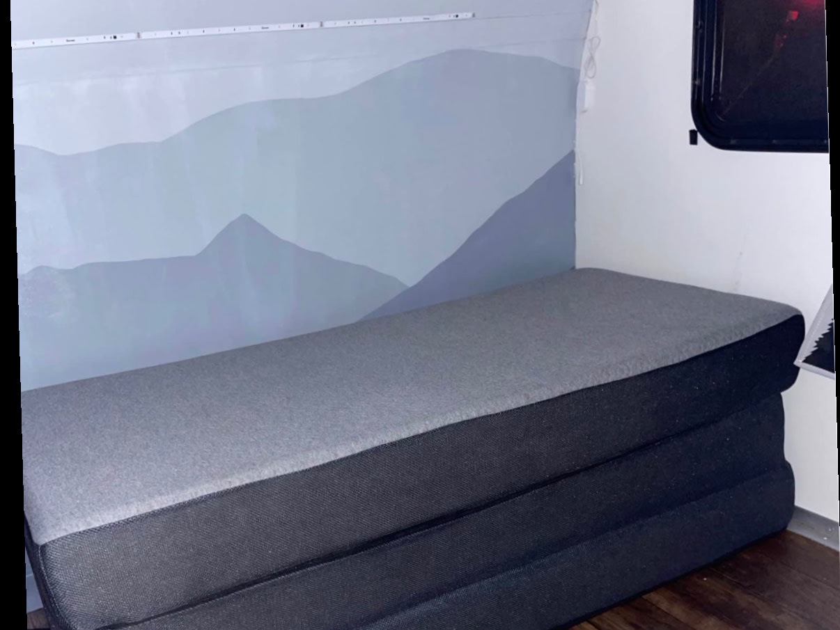 RV rental interior: A gray, three-section foldable mattress on a dark wood floor, set against a light mountain mural wall and strip lighting.. Rugged Mountain Custom RV Rustic Tear Drop Camper Koala 2022
