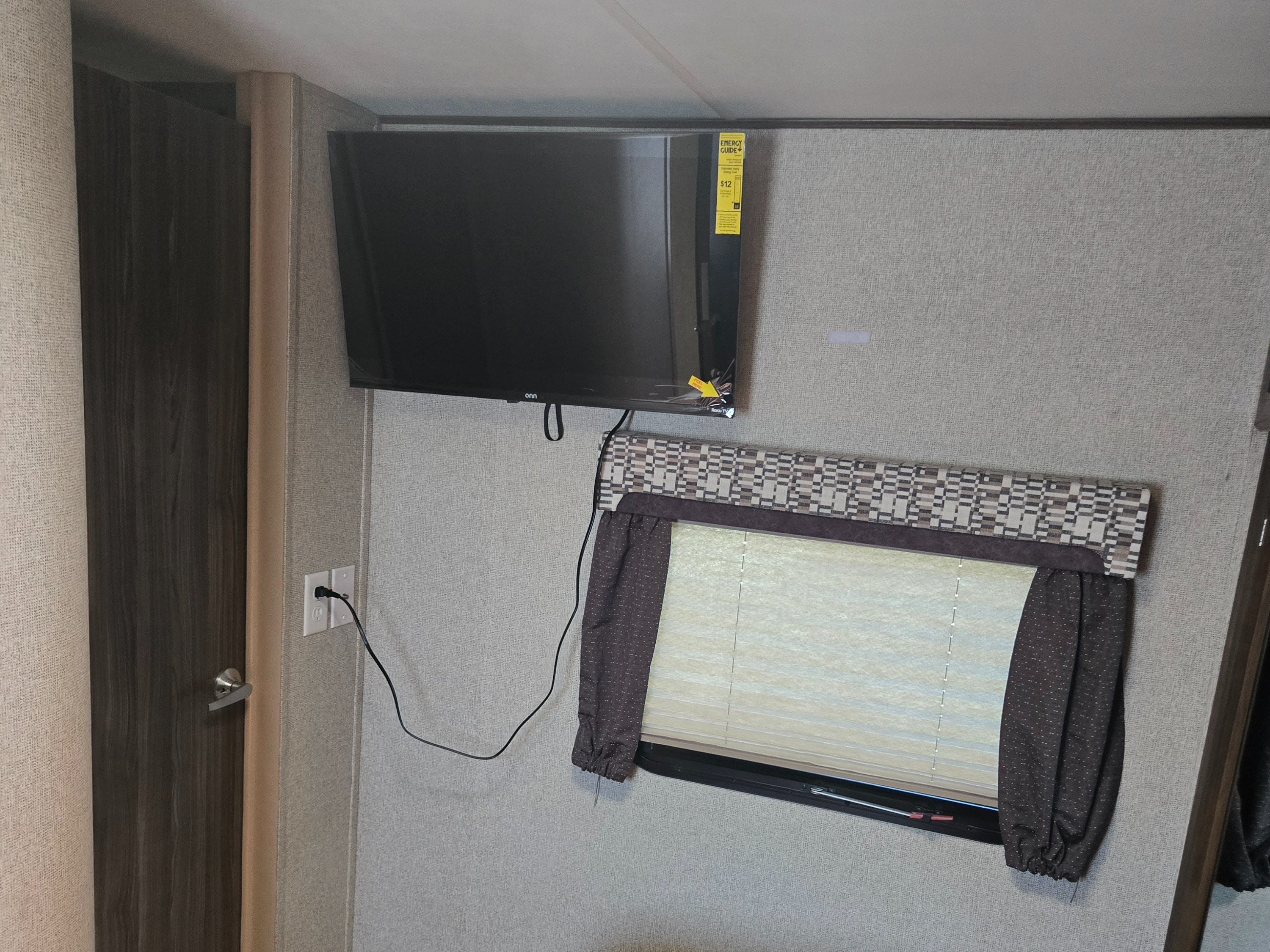 RV rental interior showcasing a wall-mounted TV, window with blinds, power outlet, and a door for a compact living area.. Coachmen Apex 2017