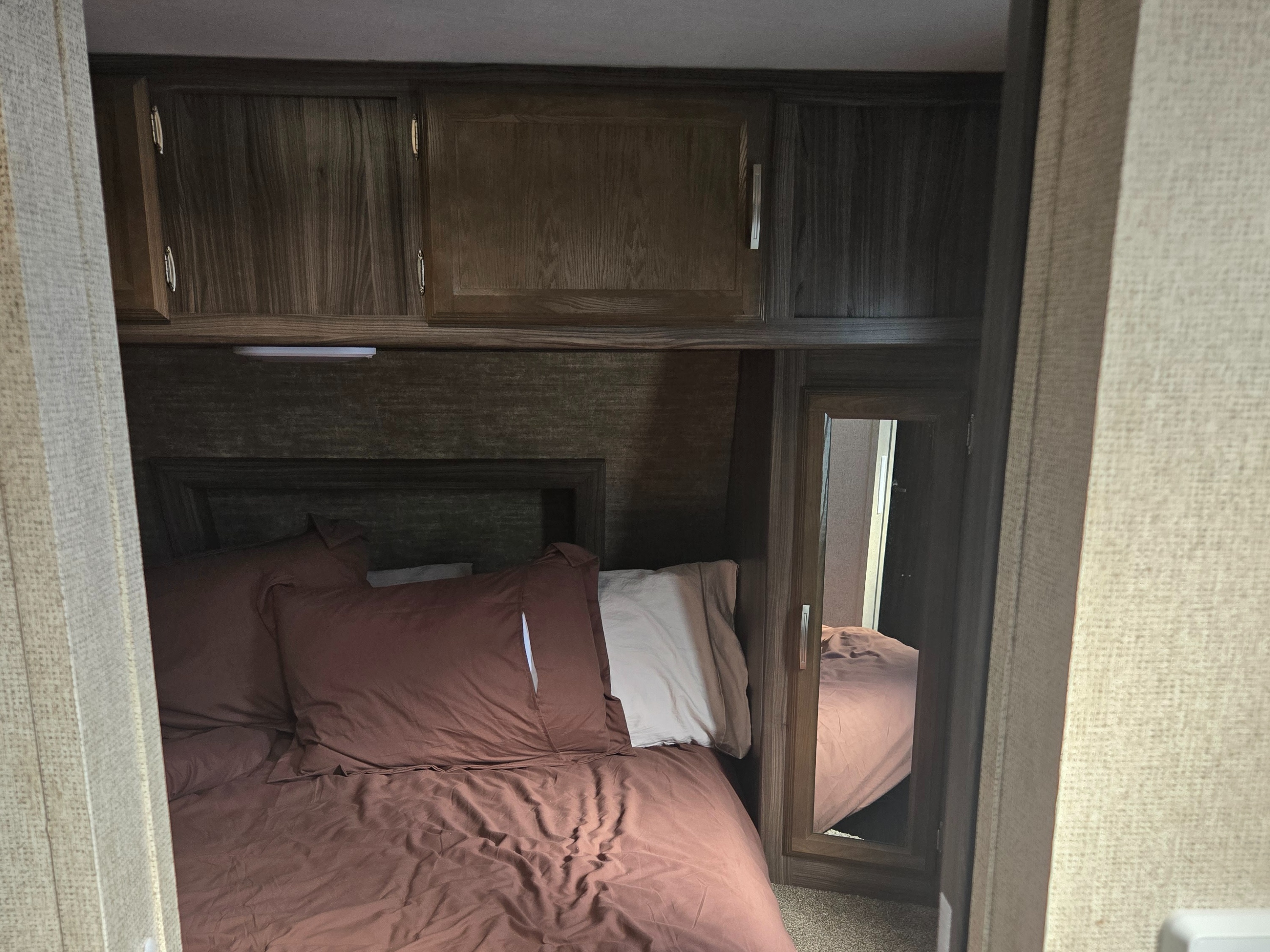 Cozy RV rental bedroom features a bed with earthy brown bedding, wooden overhead cabinets, and a mirrored wardrobe.. Coachmen Apex 2017