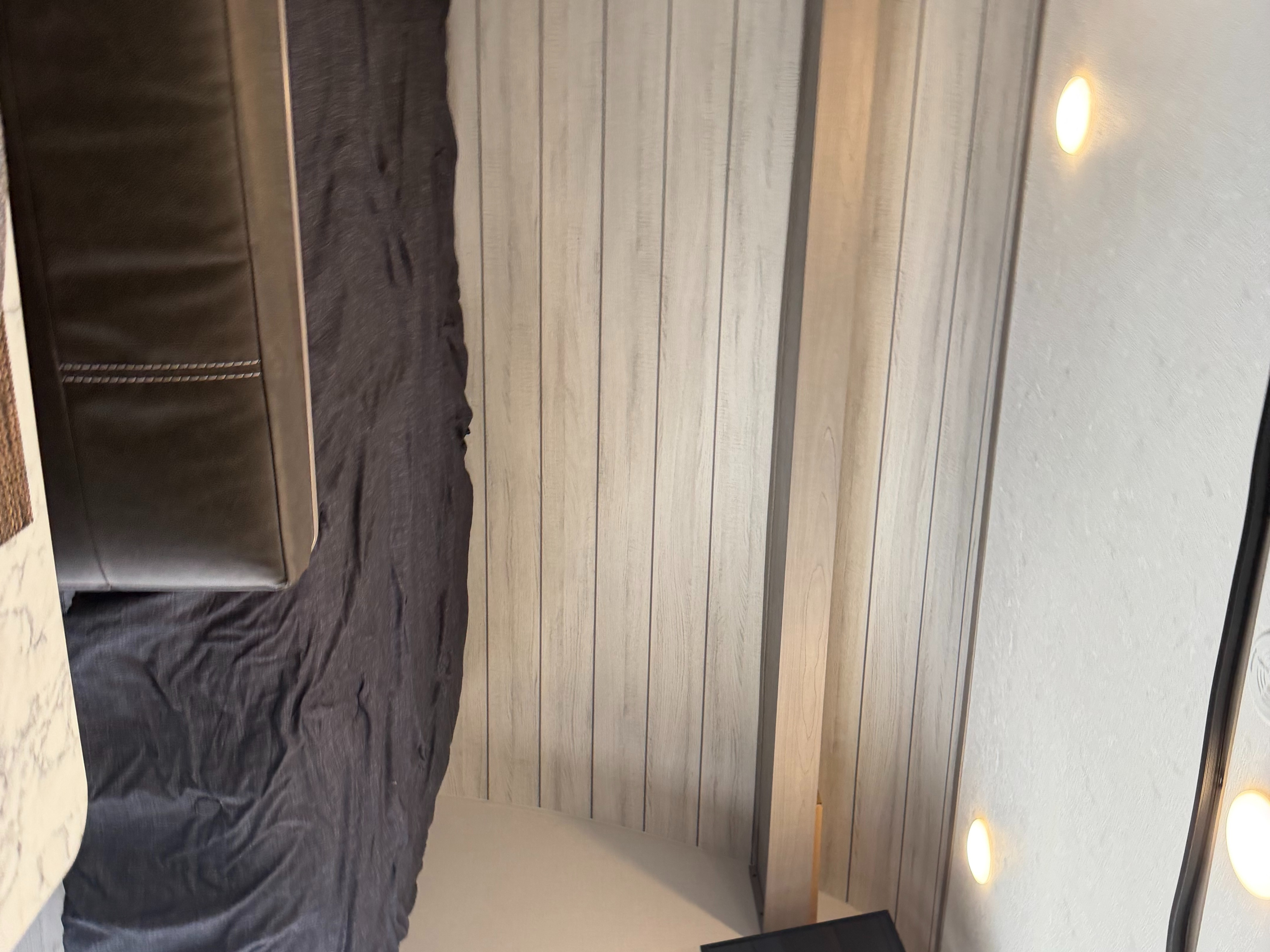 Inside an rv rental, featuring a dark grey bed, brown upholstered sofa, wood-paneled walls, and warm recessed lighting.. Keystone RV Coleman Lantern LT 17B 2024