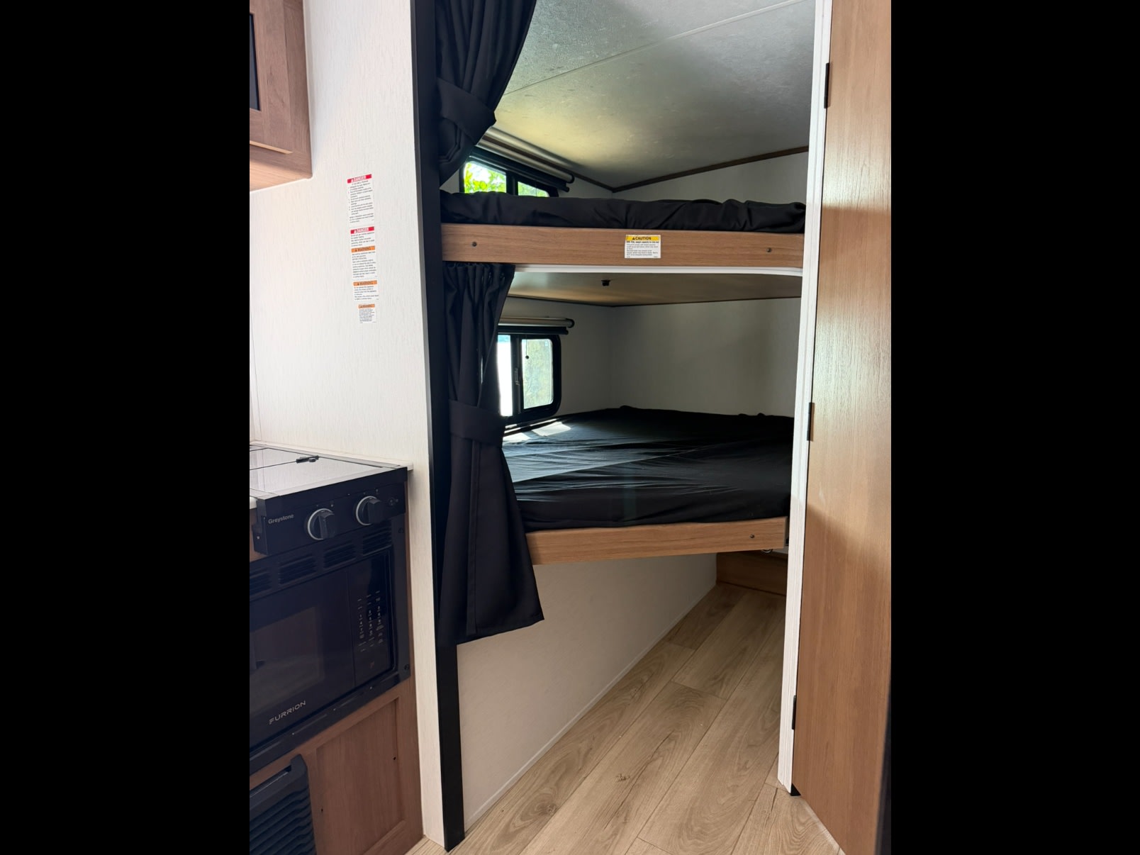 Cozy rv rental interior with bunk beds, privacy curtains, and a compact kitchen featuring a stove and microwave in a travel trailer.. Coachmen Apex Nano 2026
