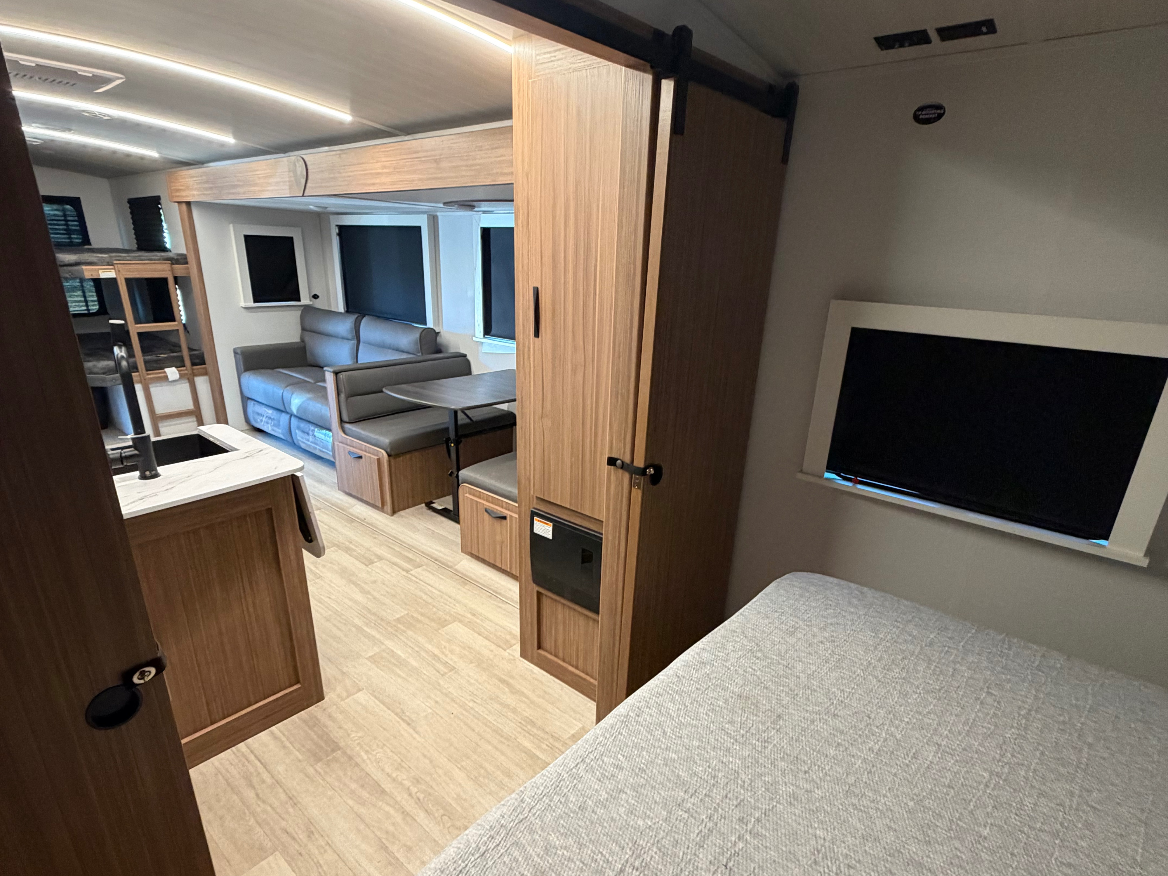 Modern rv rental interior: kitchen, dinette, bunk beds, and sleeping area with TV. Light wood and bright lighting.. Keystone RV Passport Super Lite 2025