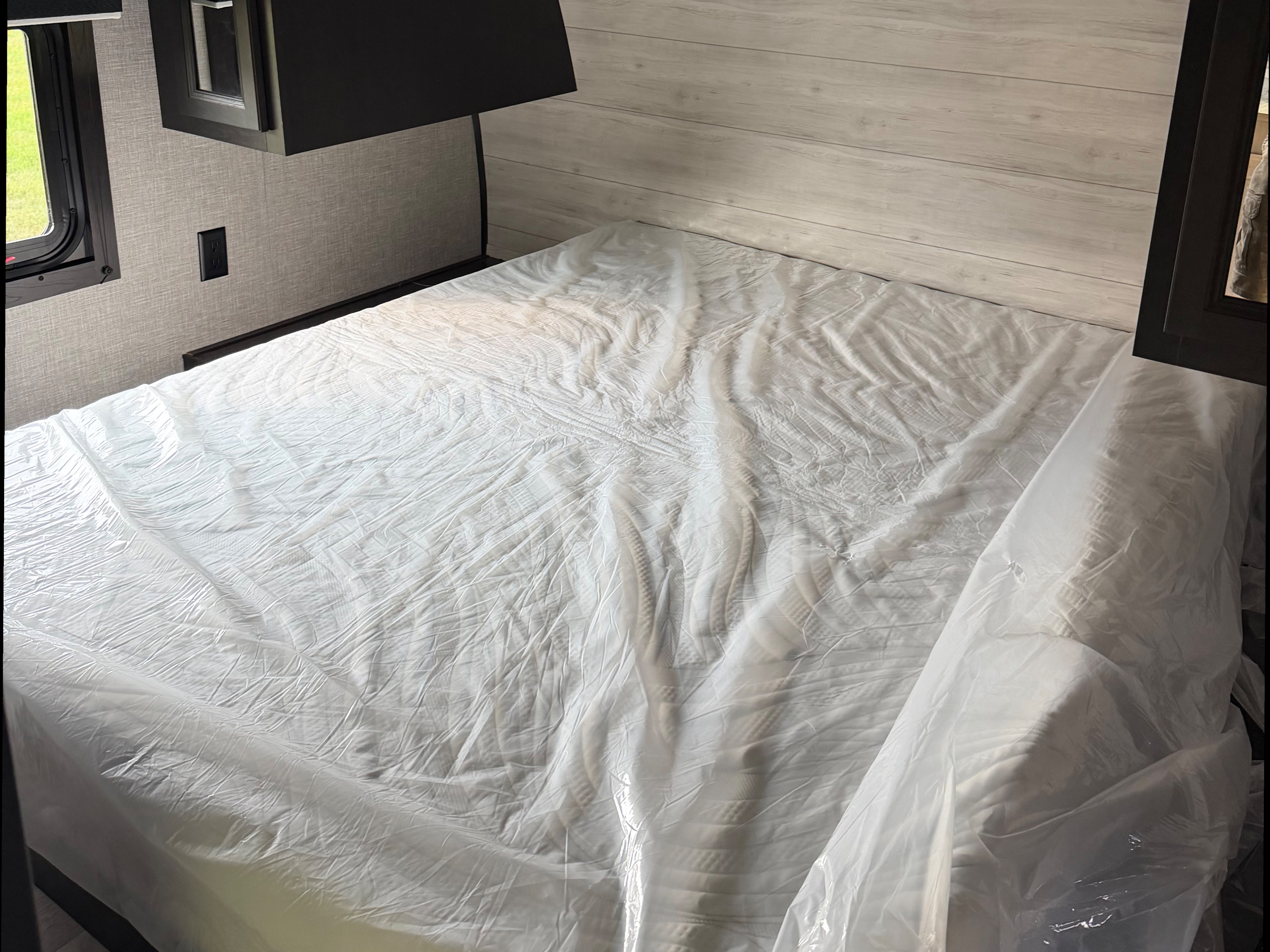 Fresh RV rental bedroom featuring a plastic-covered mattress, light wood paneling, and dark storage cabinets.. Jayco Jay Flight 2023