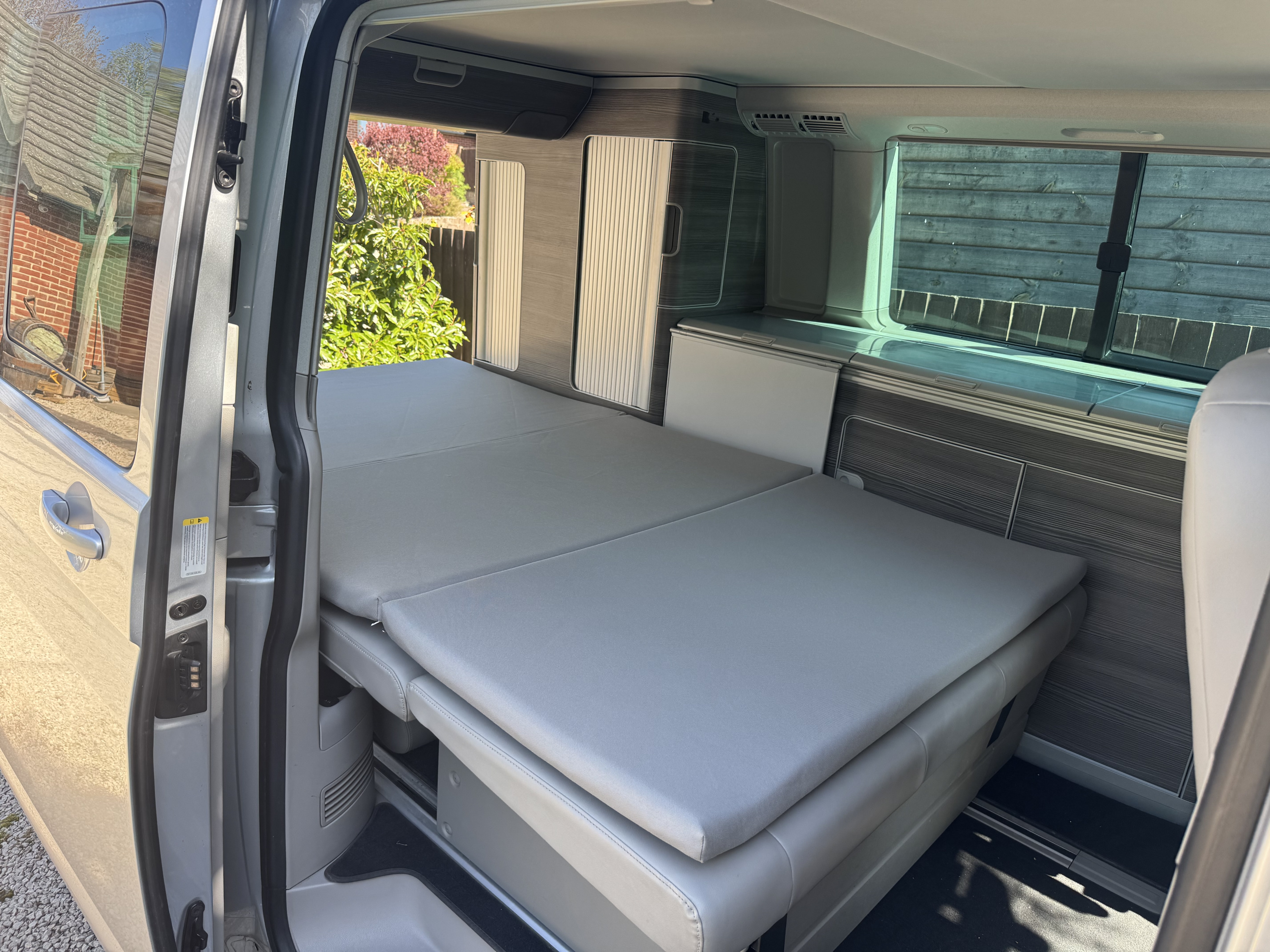RV rental: Campervan interior featuring a grey mattress bed, integrated storage, and an open side door to the outdoors.. Volkswagen california 2018