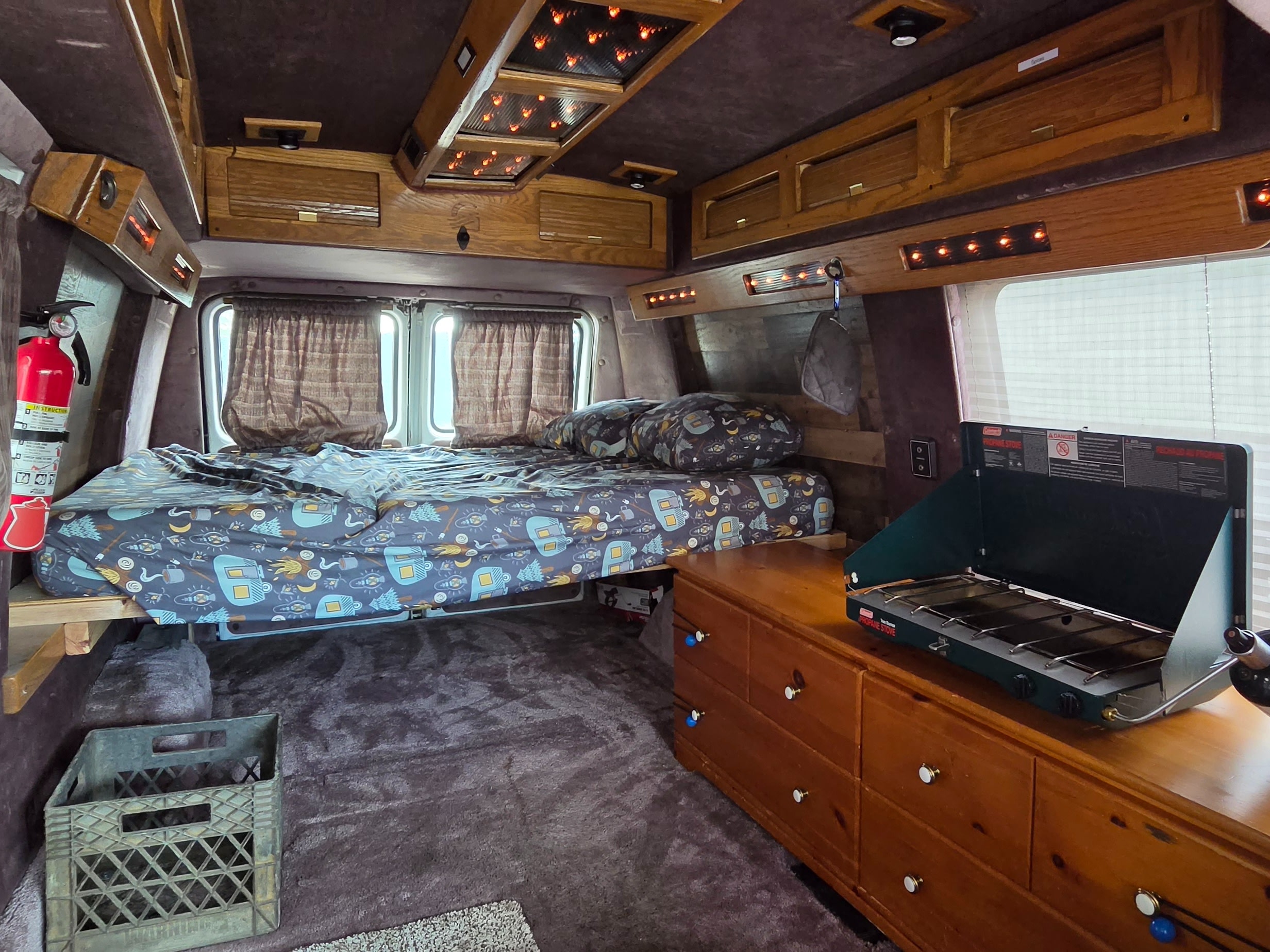 Explore this cozy RV rental interior: a bed, portable stove, and wooden cabinets for comfortable camper van adventures.. Gmc Vandura 1993