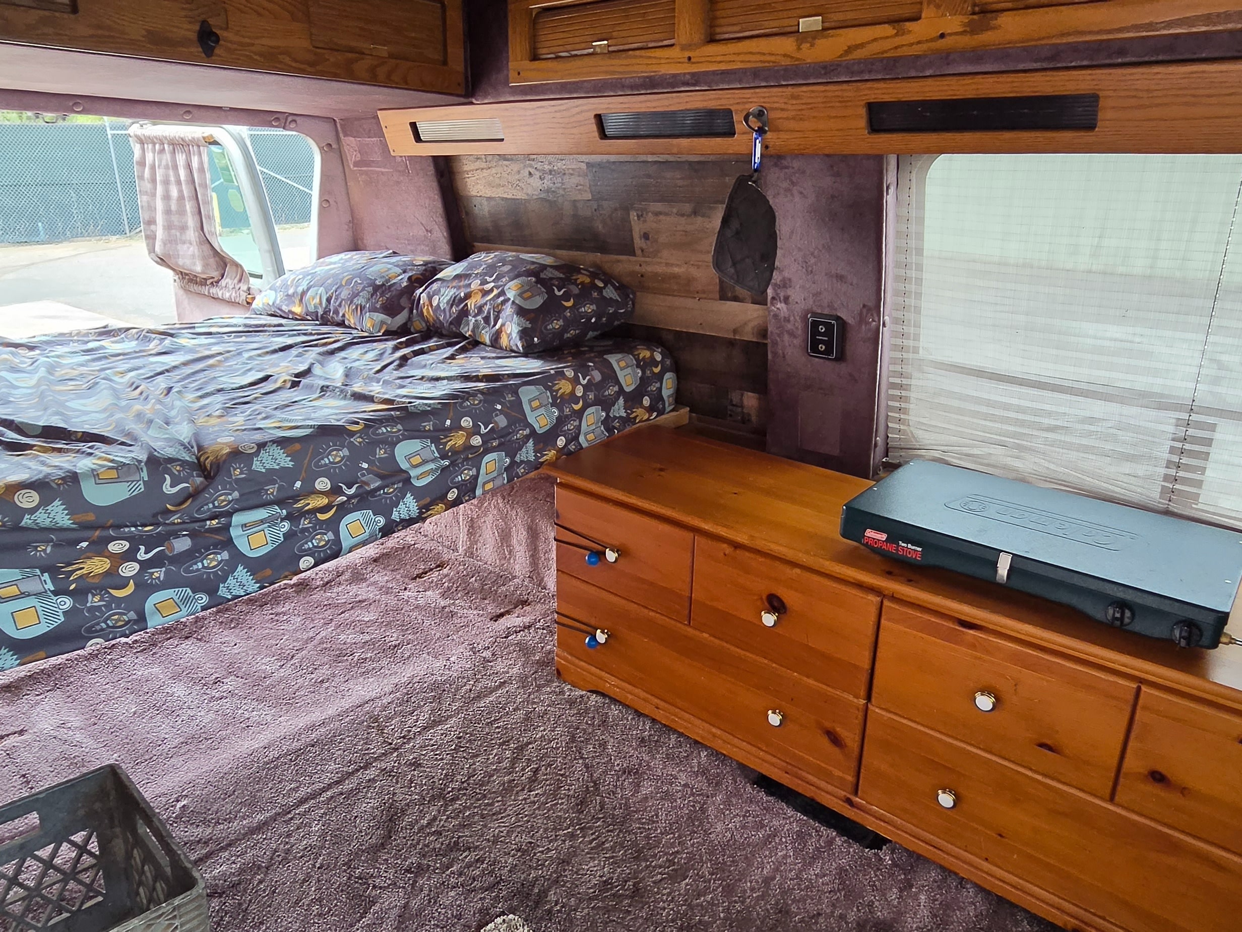 Inside an RV rental: a compact camper van setup with a cozy bed, storage, and a portable propane stove.. Gmc Vandura 1993