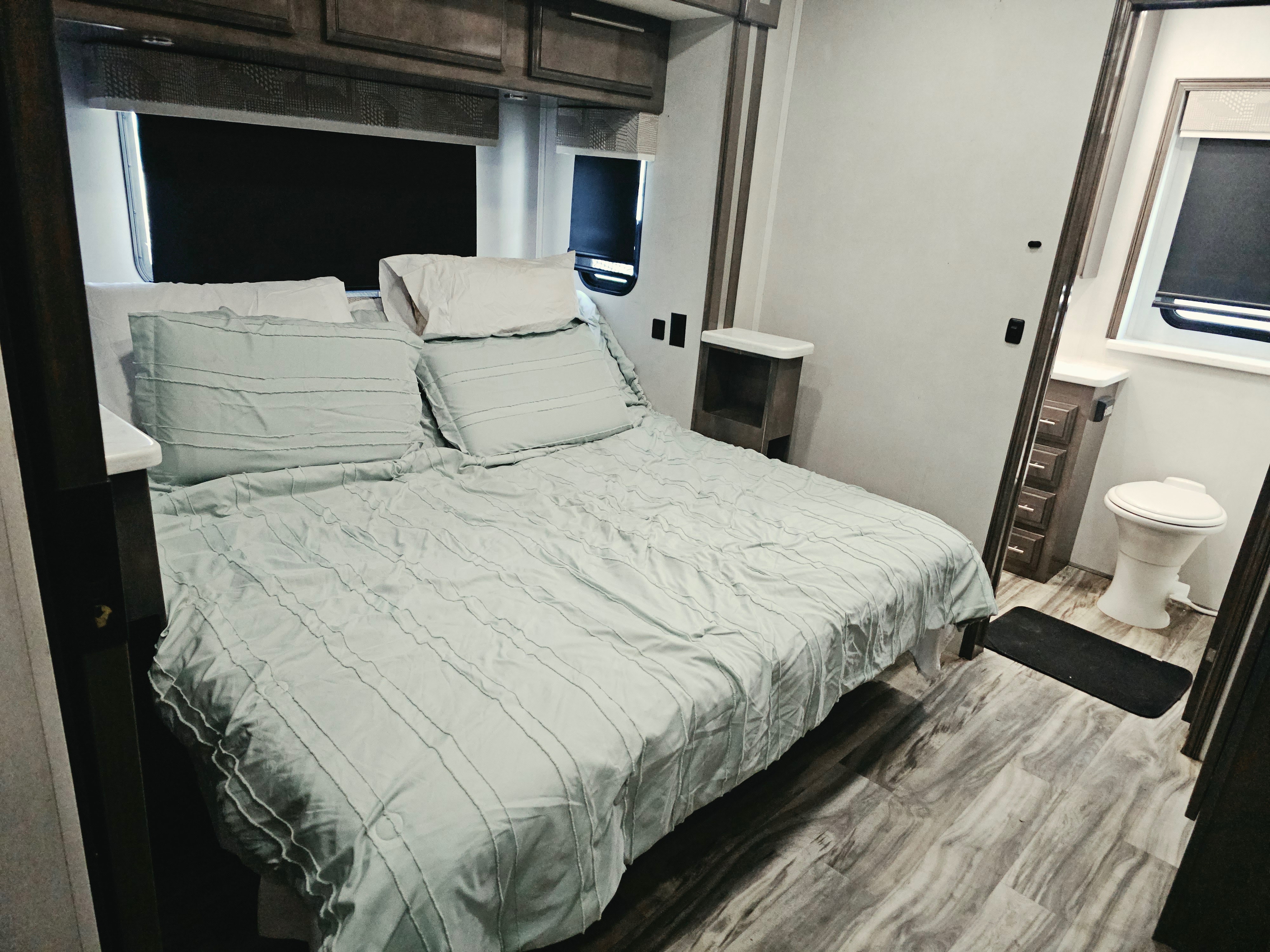 Cozy RV rental bedroom featuring a queen bed with light blue bedding, overhead cabinets, and an adjacent compact bathroom.. Georgetown GT7 2021