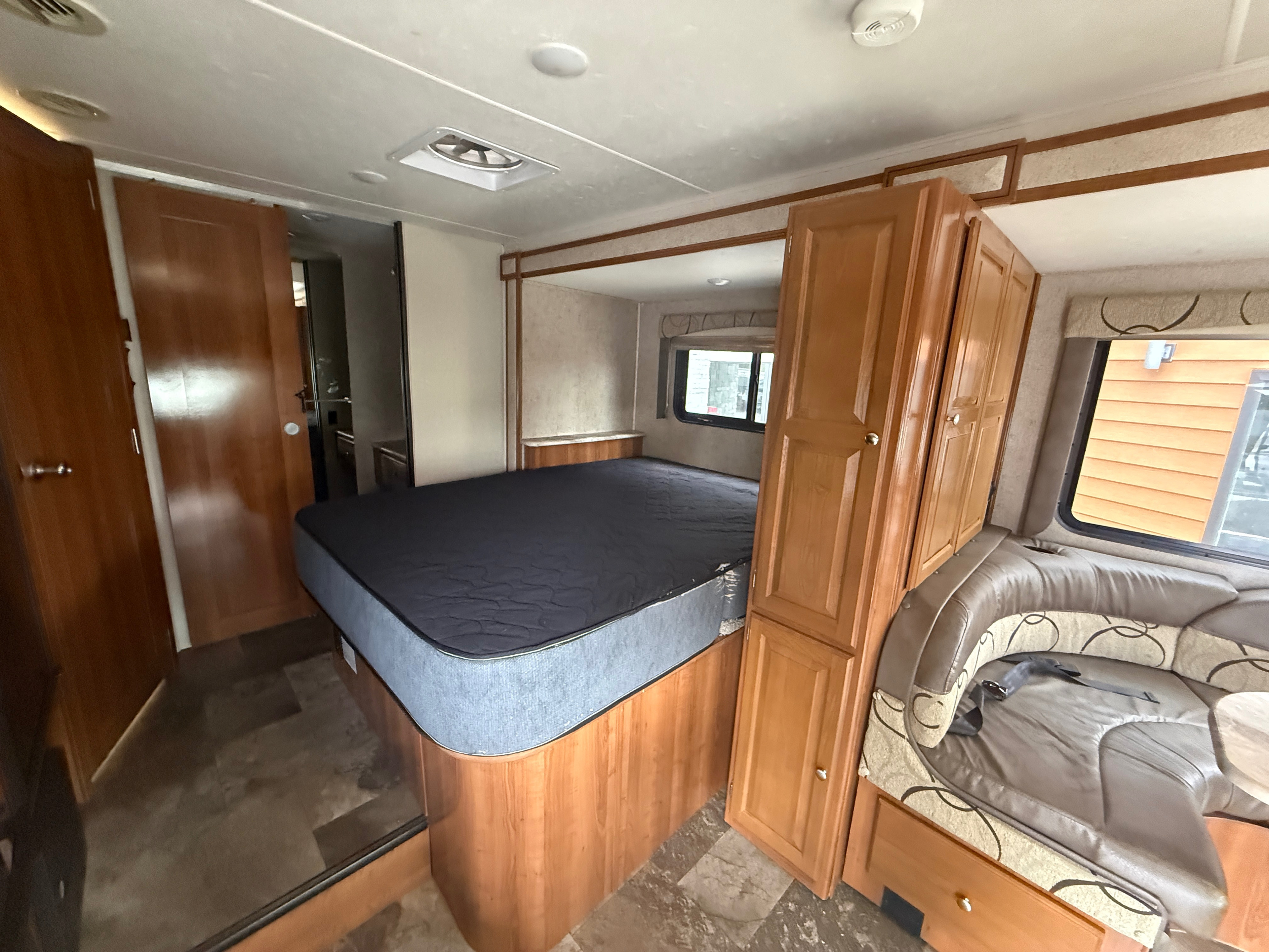 RV rental interior showcasing a comfortable queen bed, dinette seating, and wood cabinetry for a cozy stay.. Coachmen Leprechaun 240FS 2018