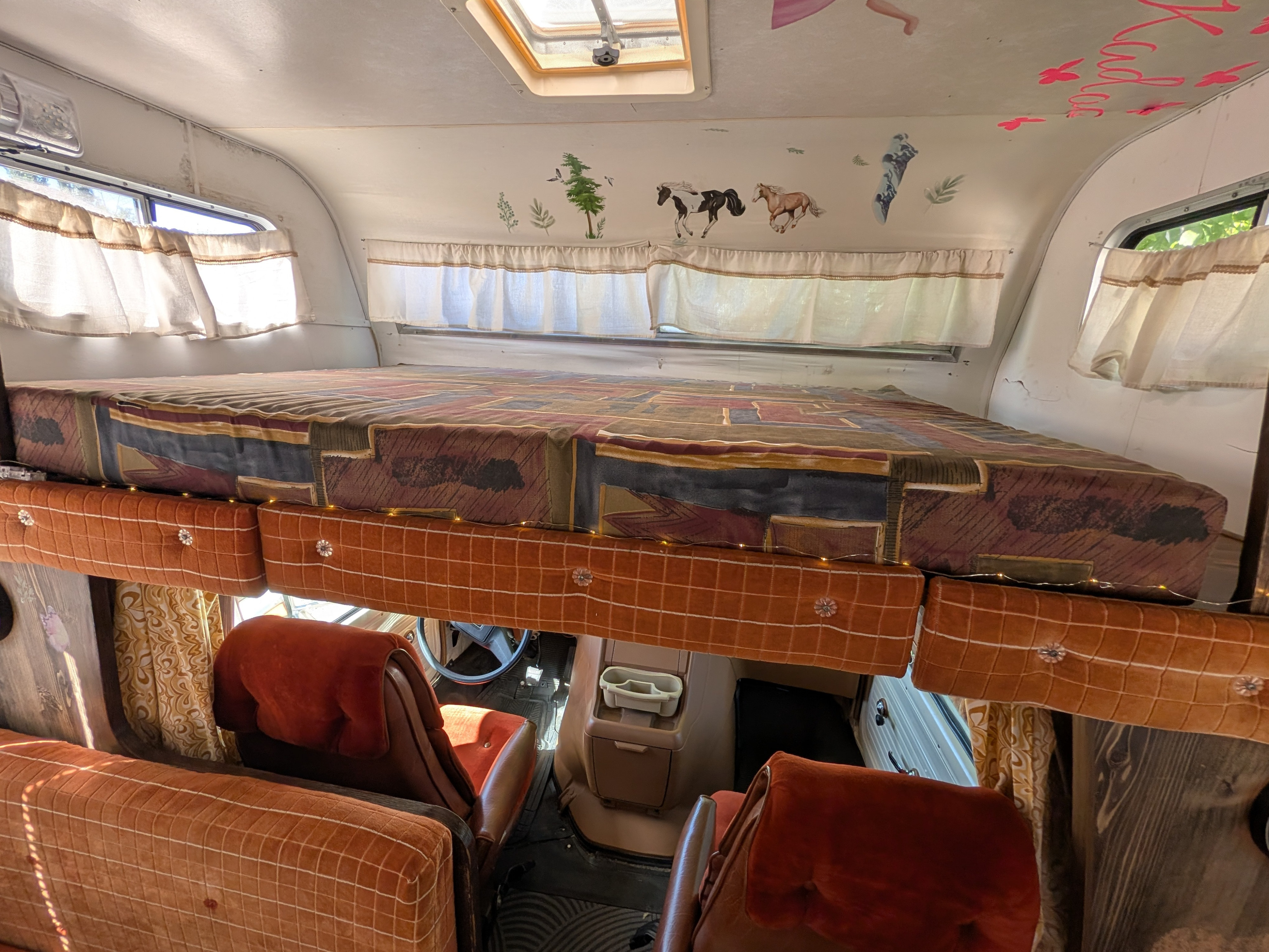Cozy RV rental interior showcasing an overhead bed with patterned bedding, cheerful wall decals, and the driver's cab below.. Chevrolet Vanguard 1980