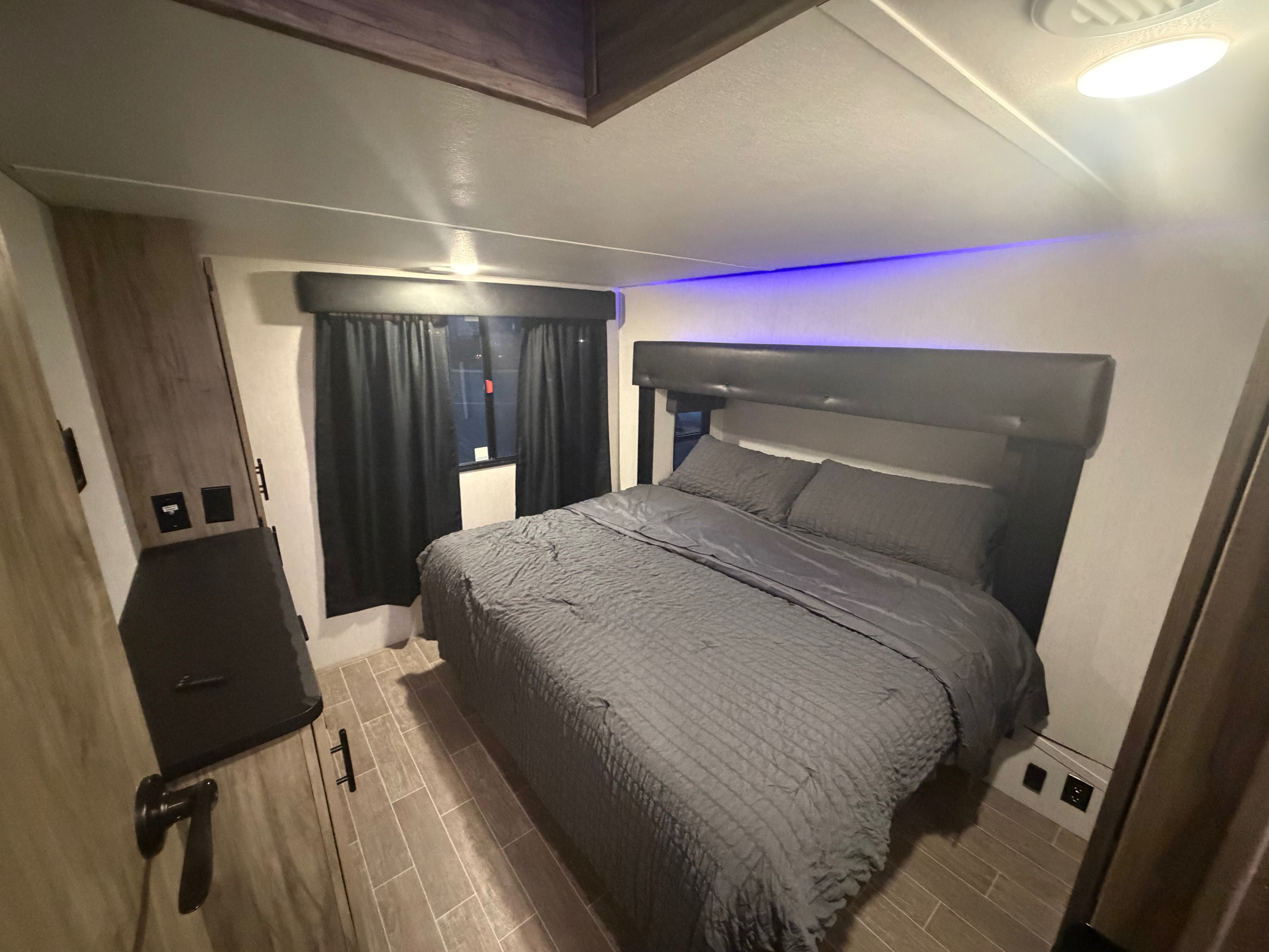 Comfortable RV rental bedroom with a large gray bed, dark curtains, and stylish blue LED lighting on the ceiling.. Forest River Cherokee Arctic Wolf 2022