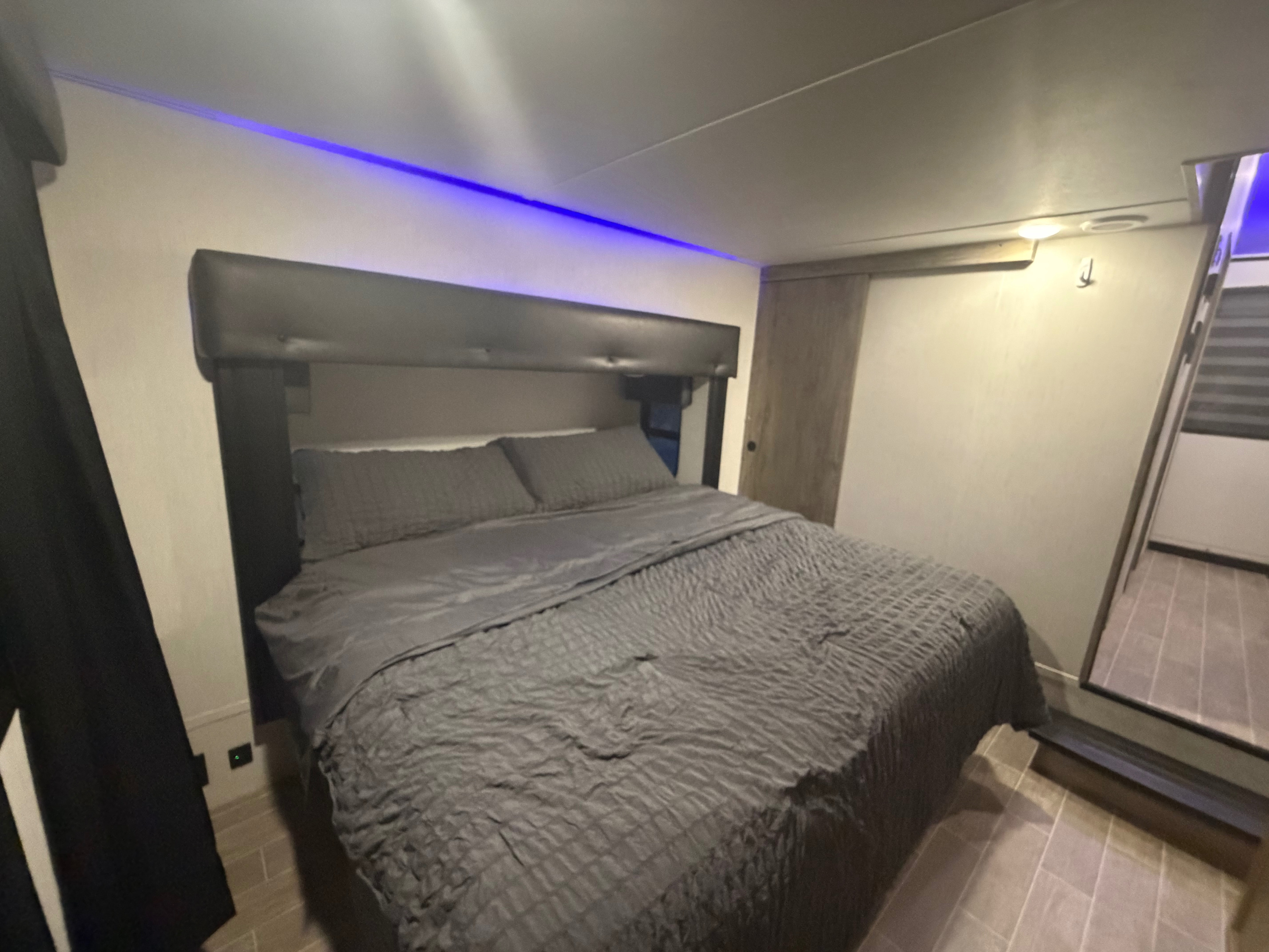 Cozy RV rental bedroom featuring a modern gray bed, blue ambient lighting above the headboard, and wood-look flooring.. Forest River Cherokee Arctic Wolf 2022