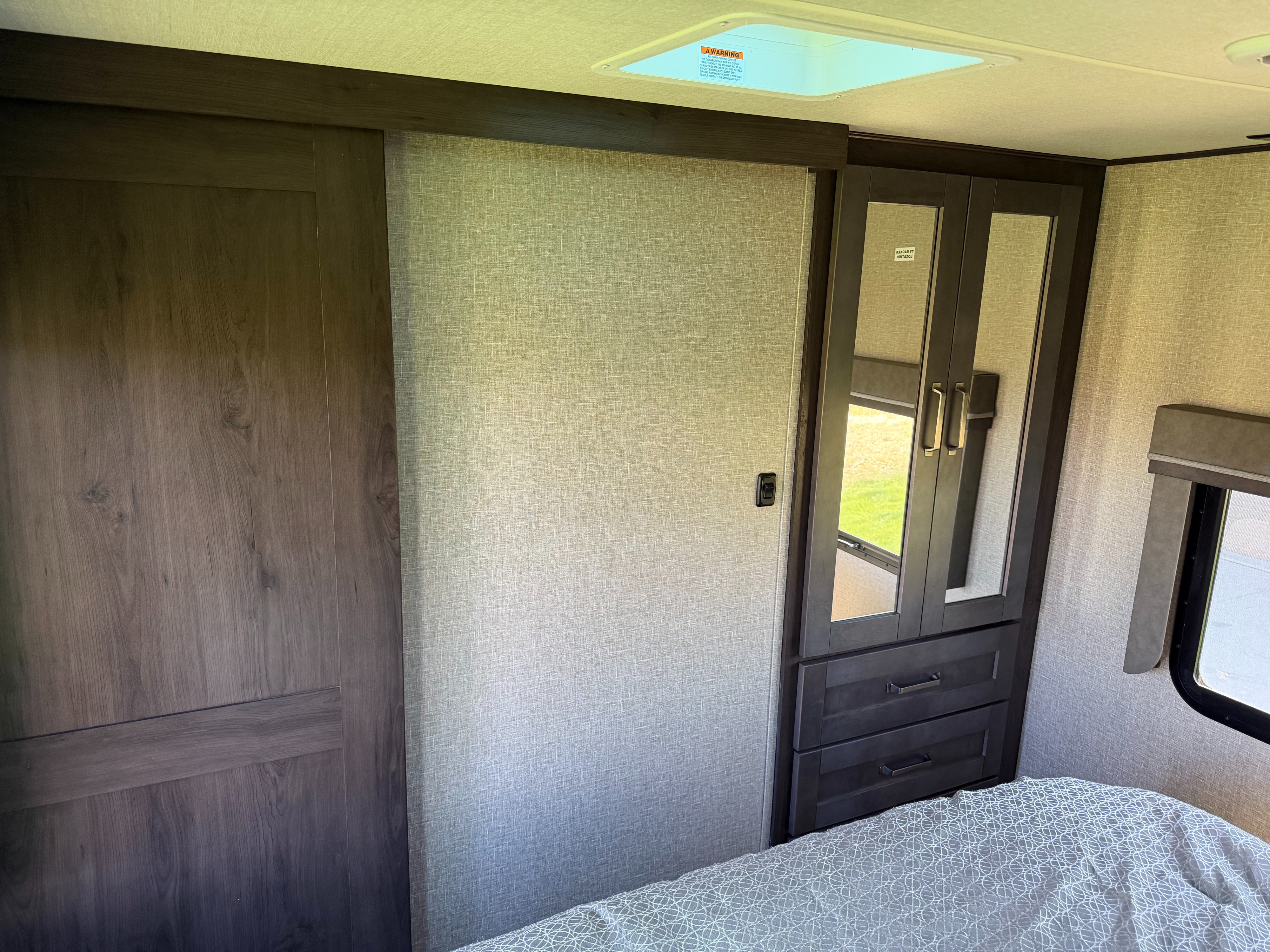 Modern RV rental bedroom with textured wall, sliding door, mirrored wardrobe, bed, and skylight.. Grand Design Reflection 2022