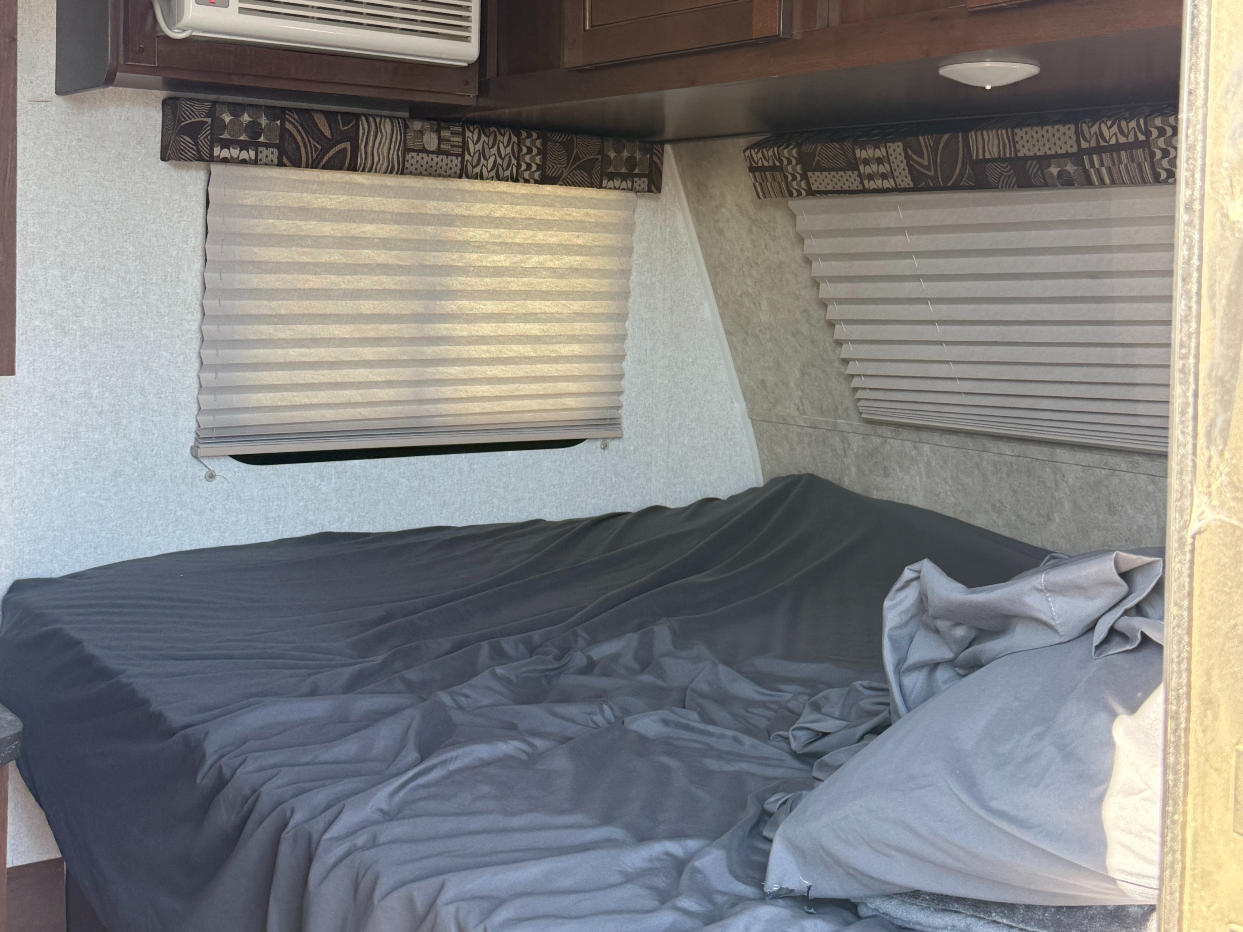 Comfortable RV rental bedroom: made bed with gray sheets, windows with blinds, and AC unit overhead.. Jayco Jay Flight SLX 2017