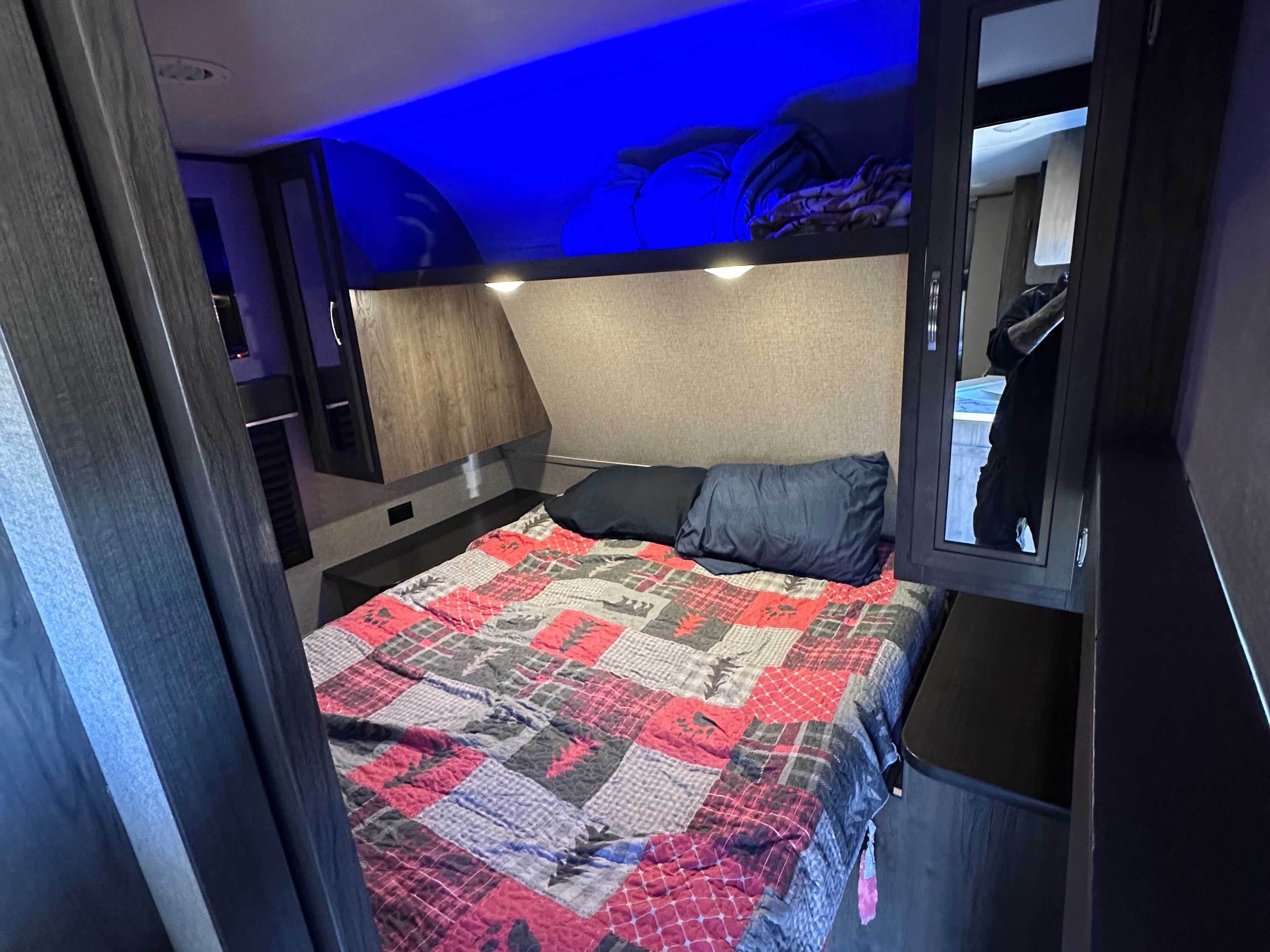 This cozy rv rental bedroom offers a comfortable bed with a unique patterned quilt, overhead storage, and blue accent lighting.. Jayco Jay Flight SLX Rocky Mountain Edition 2020