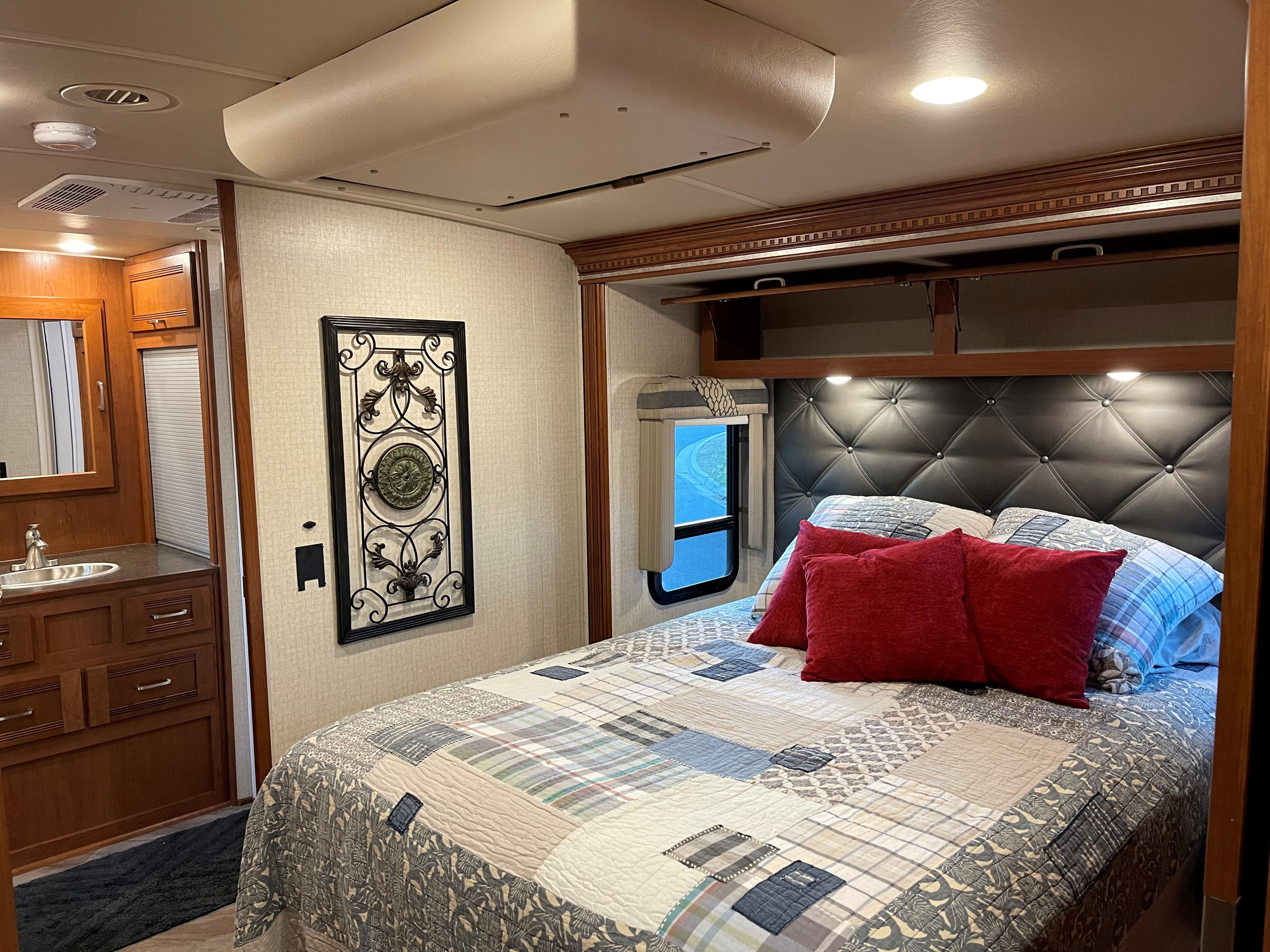 This inviting RV rental bedroom features a cozy bed with a patterned quilt, tufted headboard, overhead storage, and a small vanity.. Winnebago Forza 2017