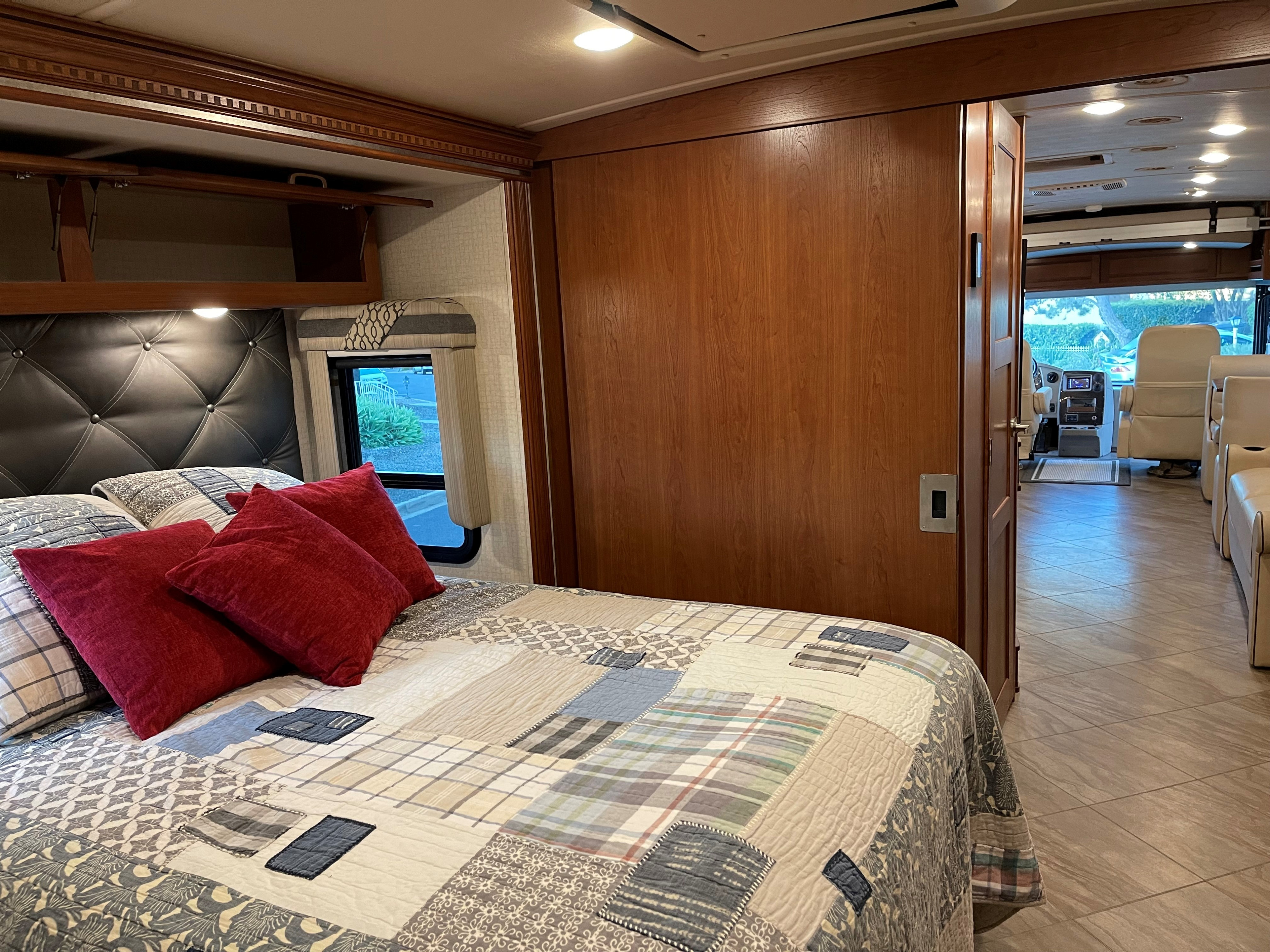 Cozy RV rental bedroom with patchwork quilt, red pillows, and sliding door open to the living area and cockpit. Ideal for travel.. Winnebago Forza 2017