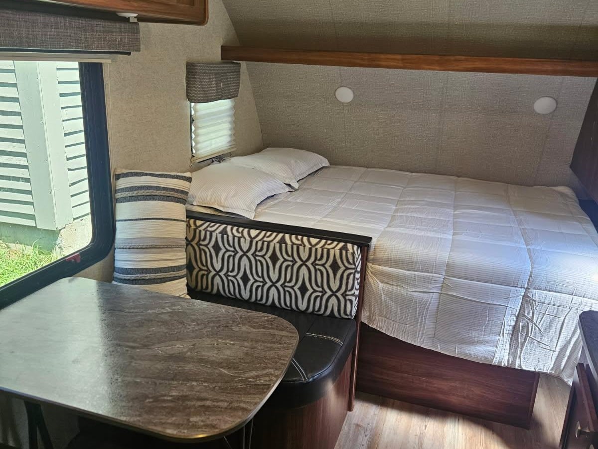 Cozy RV rental interior featuring a bed, dinette, and window view. Perfect for travel trailer adventures.. Heartland RVs Mallard 2018