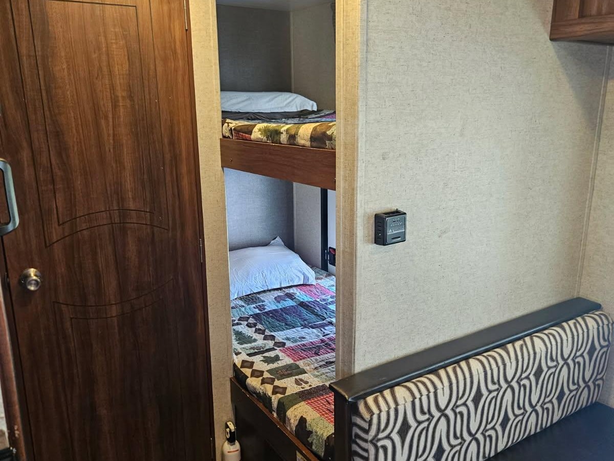 RV rental interior: bunk beds with patterned quilts, a wooden door, and a bench seat with a black and white wavy design.. Heartland RVs Mallard 2018