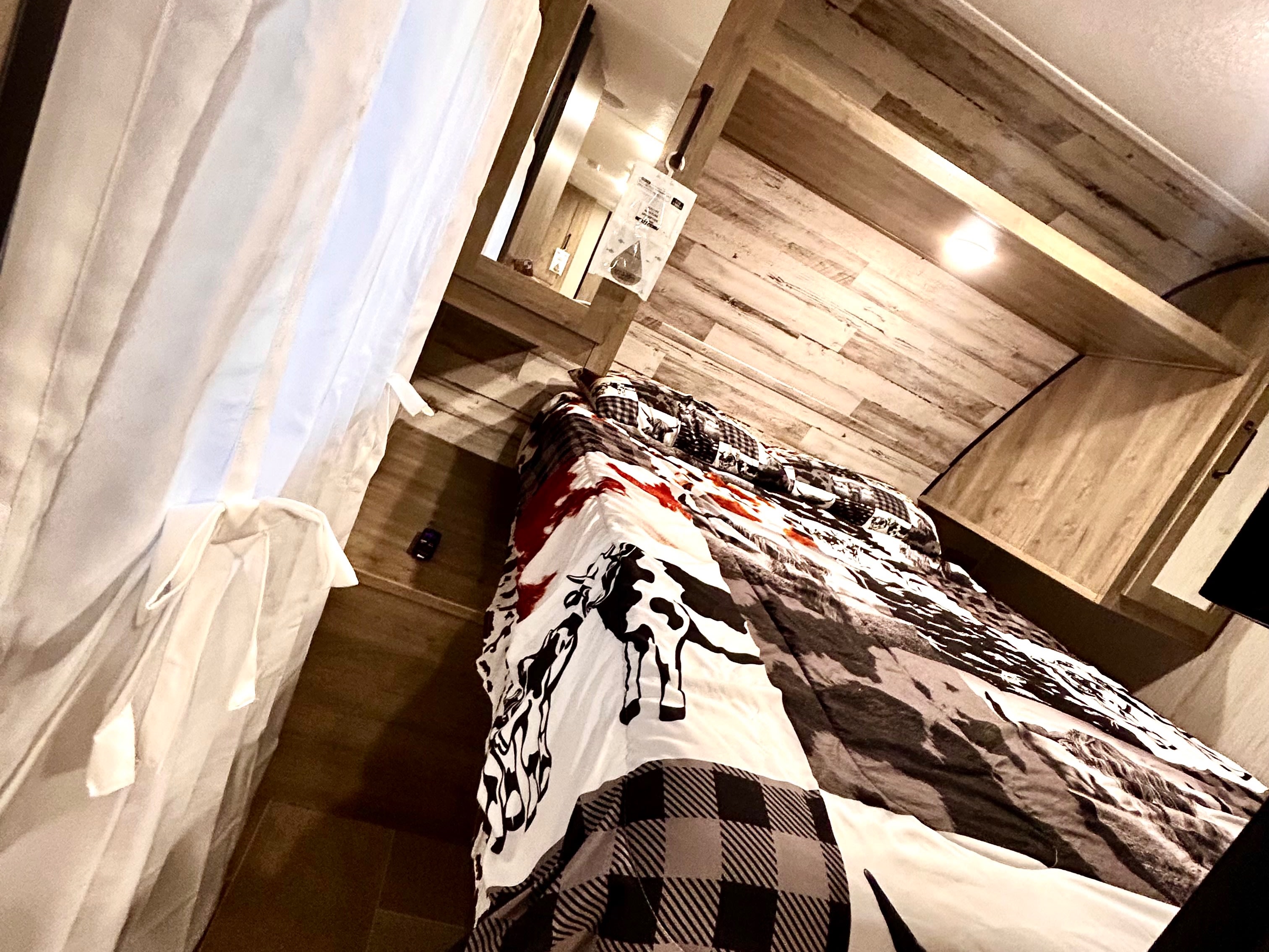 Cozy RV rental bedroom with unique cow print & plaid bedding, wooden walls, and soft lighting for a comfortable stay.. Forest River Palomino Puma XLE Lite 2021