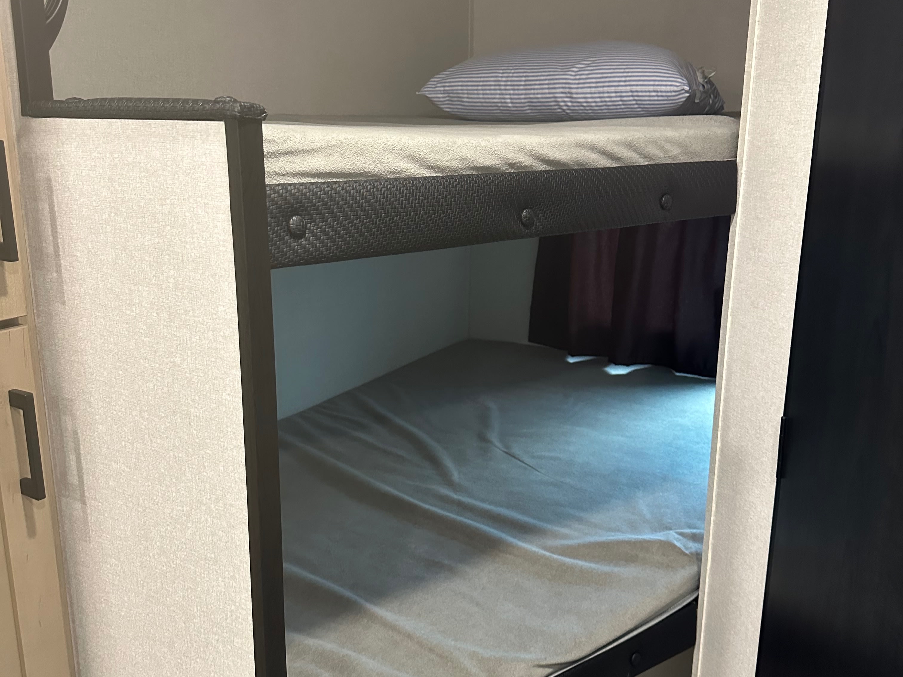 Interior of an RV rental showing bunk beds: a top bunk with a blue striped pillow and a lower bunk with grey bedding.. Jayco Jay Flight SLX 2026