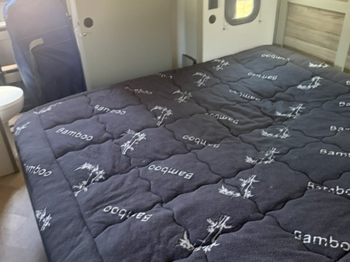 RV rental bed with a quilted "Bamboo" mattress pad, offering comfort in this camper's interior. Toilet visible.. Keystone RV Sprinter 2025
