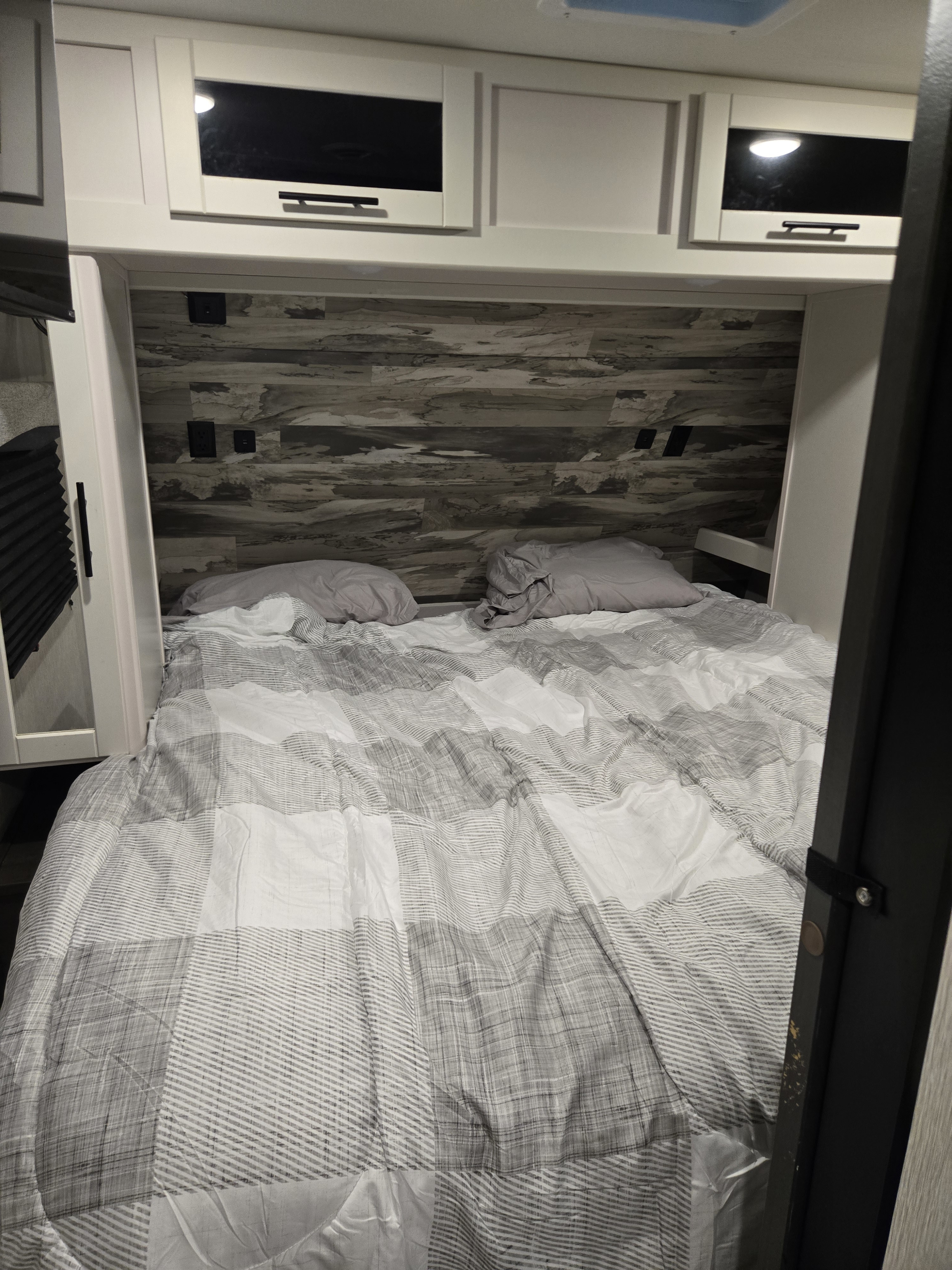 RV rental bedroom: a bed with striped comforter, wood-look headboard, and white overhead cabinets.. Crossroads RV Cruiser Aire 2024