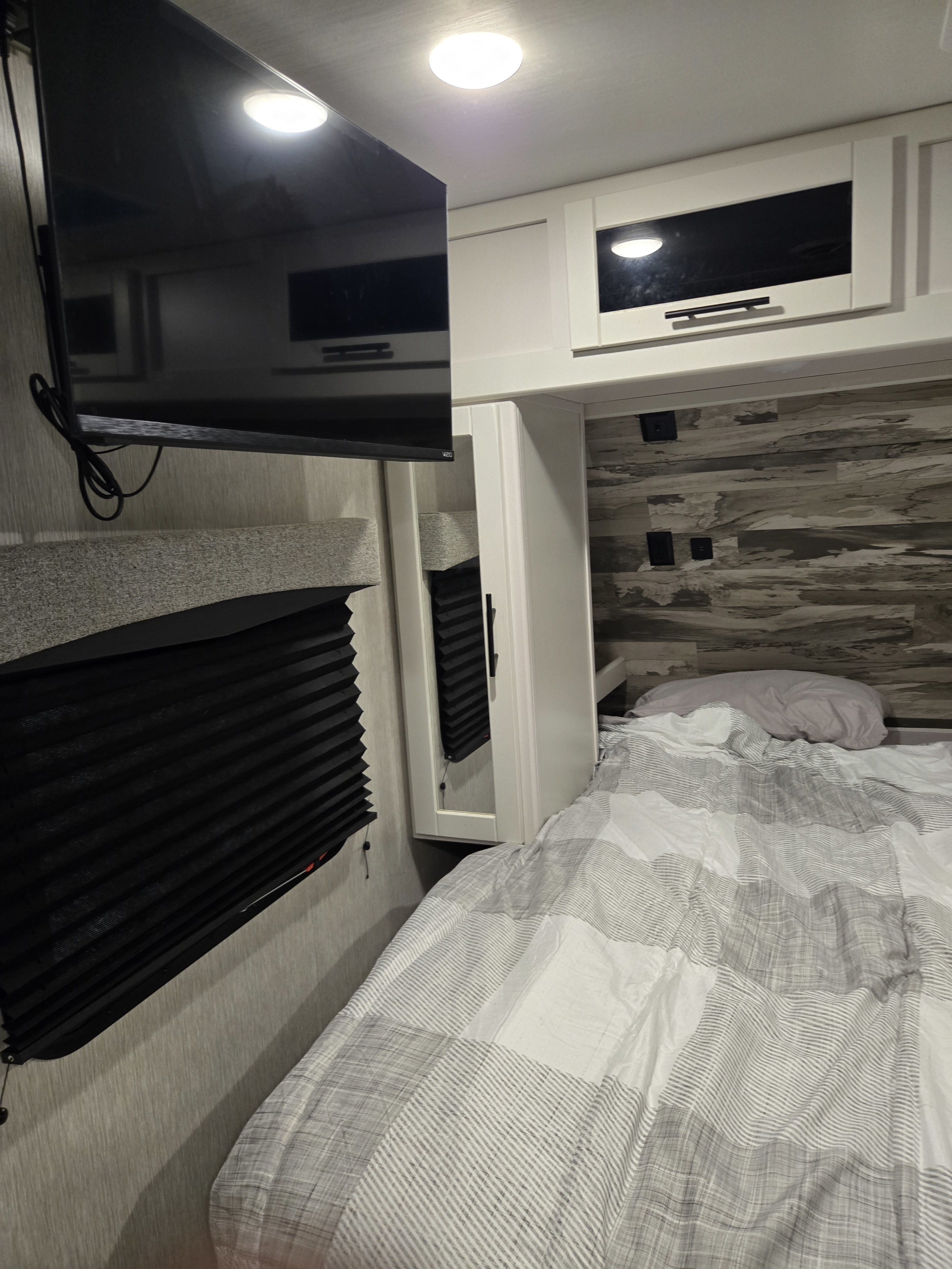 RV rental bedroom: a cozy retreat with a bed featuring striped bedding, a wall-mounted TV, and overhead cabinets.. Crossroads RV Cruiser Aire 2024