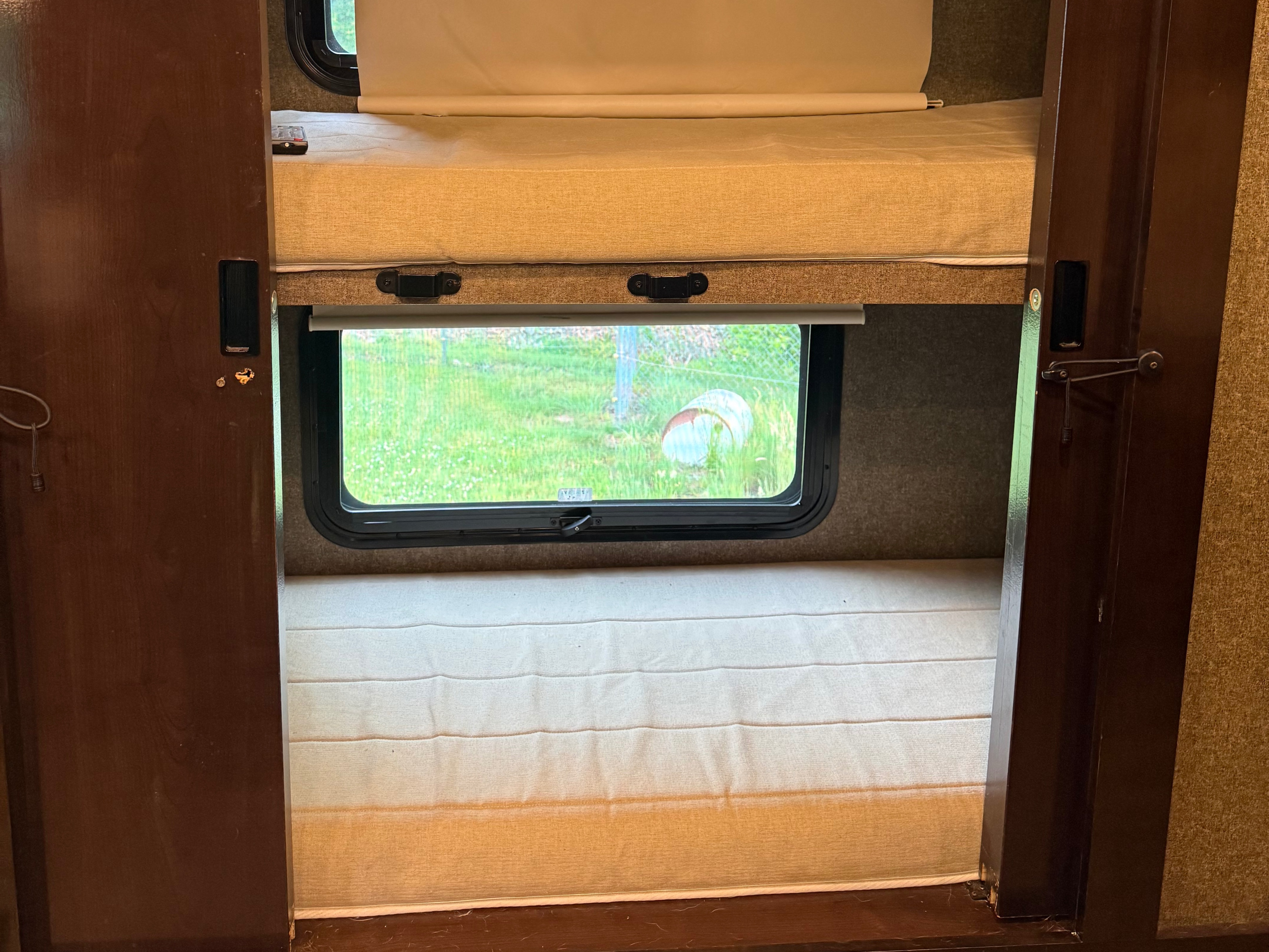 Inside an RV rental: bunk beds, window with green view, and privacy blinds. A comfortable sleeping area.. Thor Miramar 2019