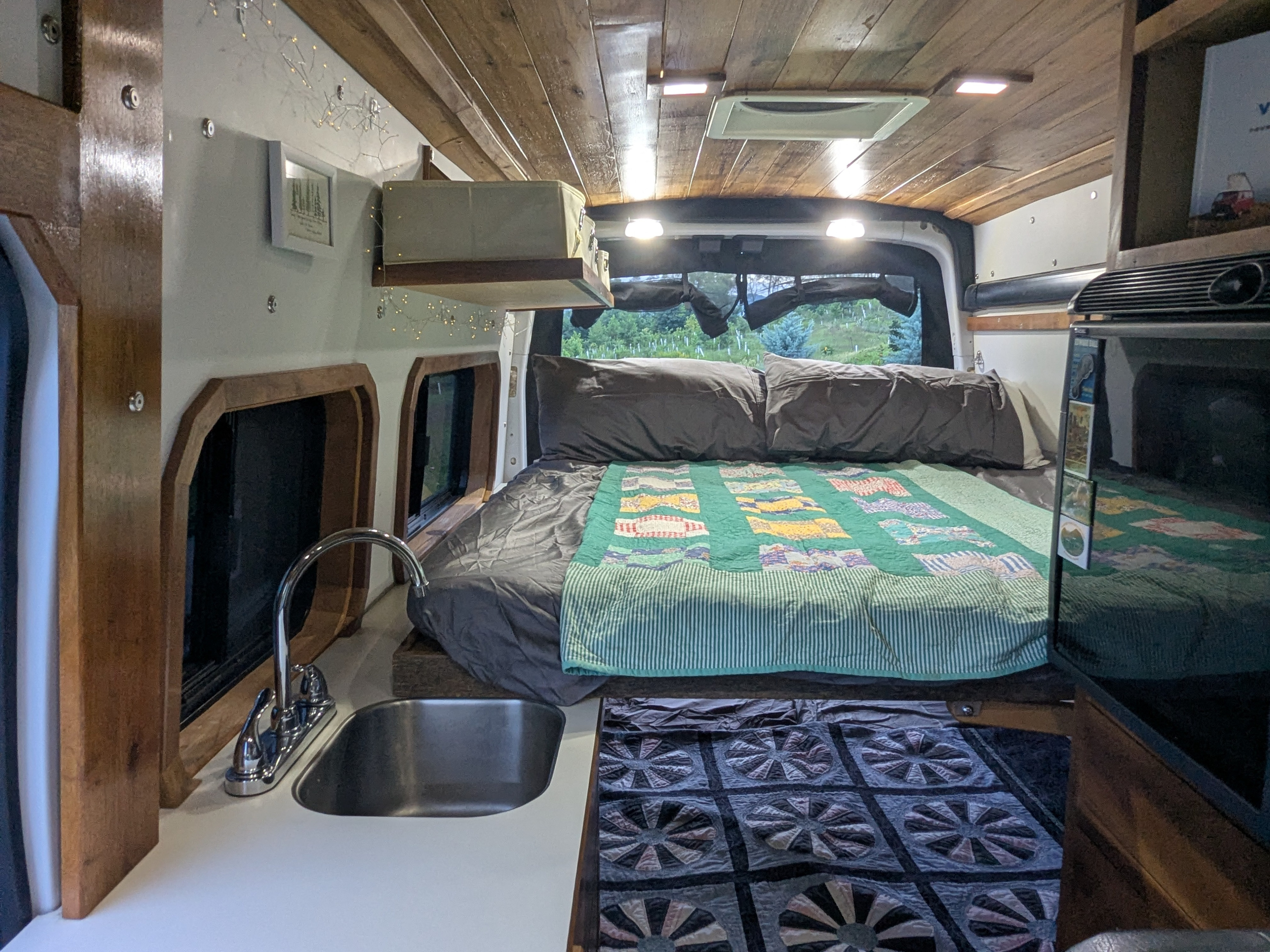 Inside a cozy RV rental: a bed with quilts, small kitchen sink, wood ceiling, and fairy lights for a warm travel experience.. Ford Transit custom 2018