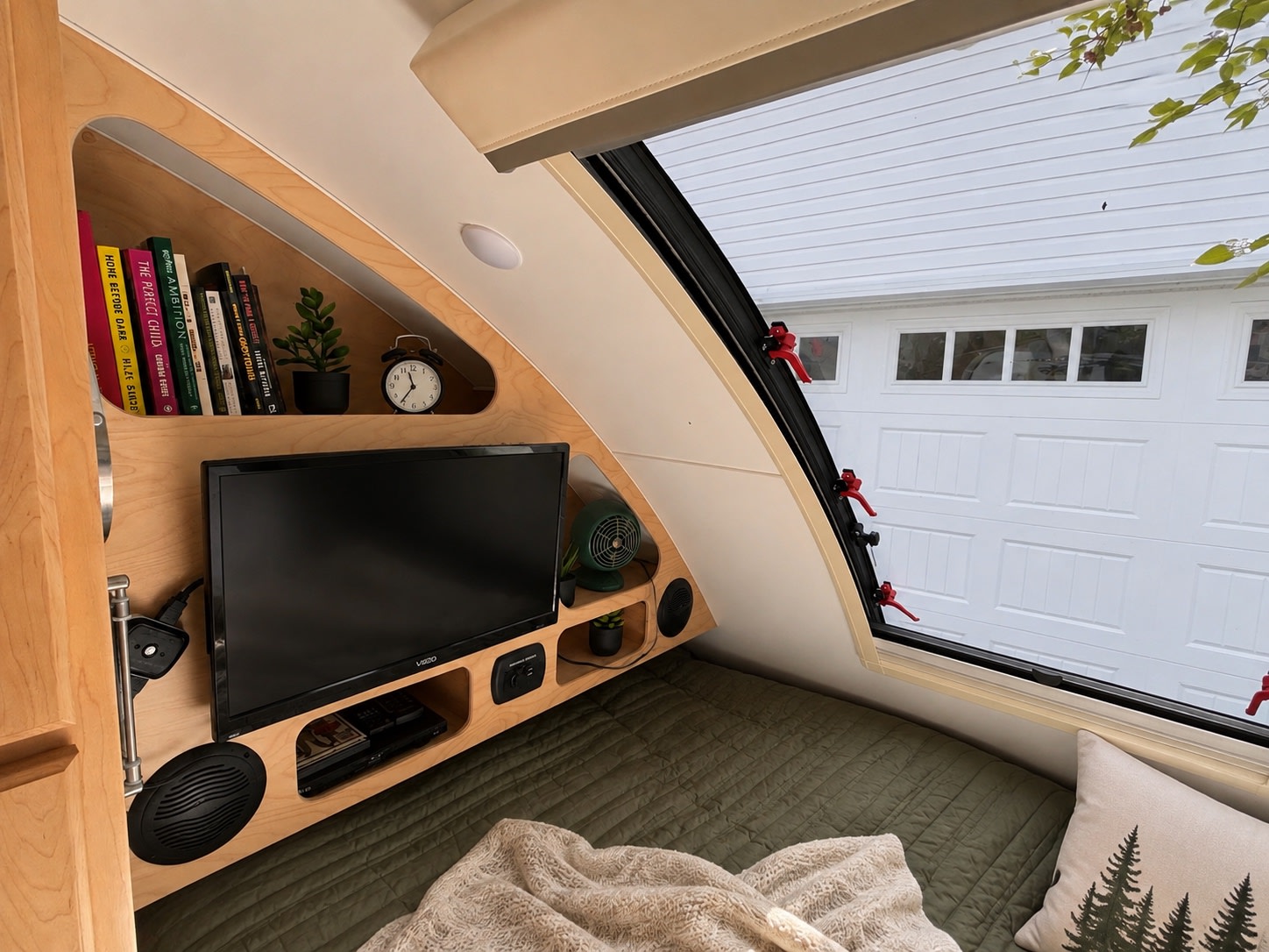 Cozy rv rental interior: compact bed area with built-in wooden shelves, books, TV, and window. Ideal for your next trip.. Little Guy Little Guy Trailer 2023