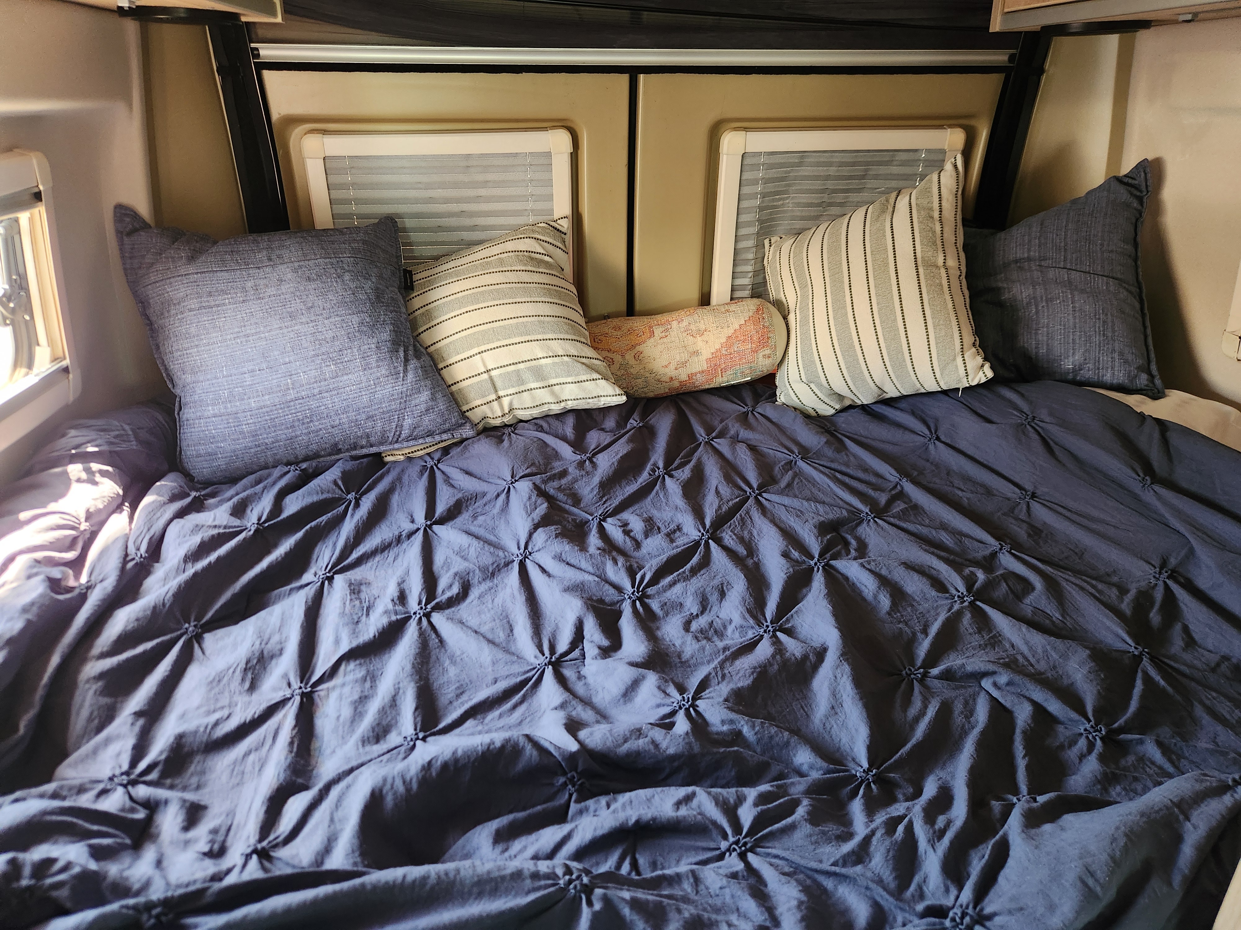 Comfortable sleeping setup in an RV rental, featuring a blue tufted comforter & assorted throw pillows.. RAM ProMaster 3500 2016