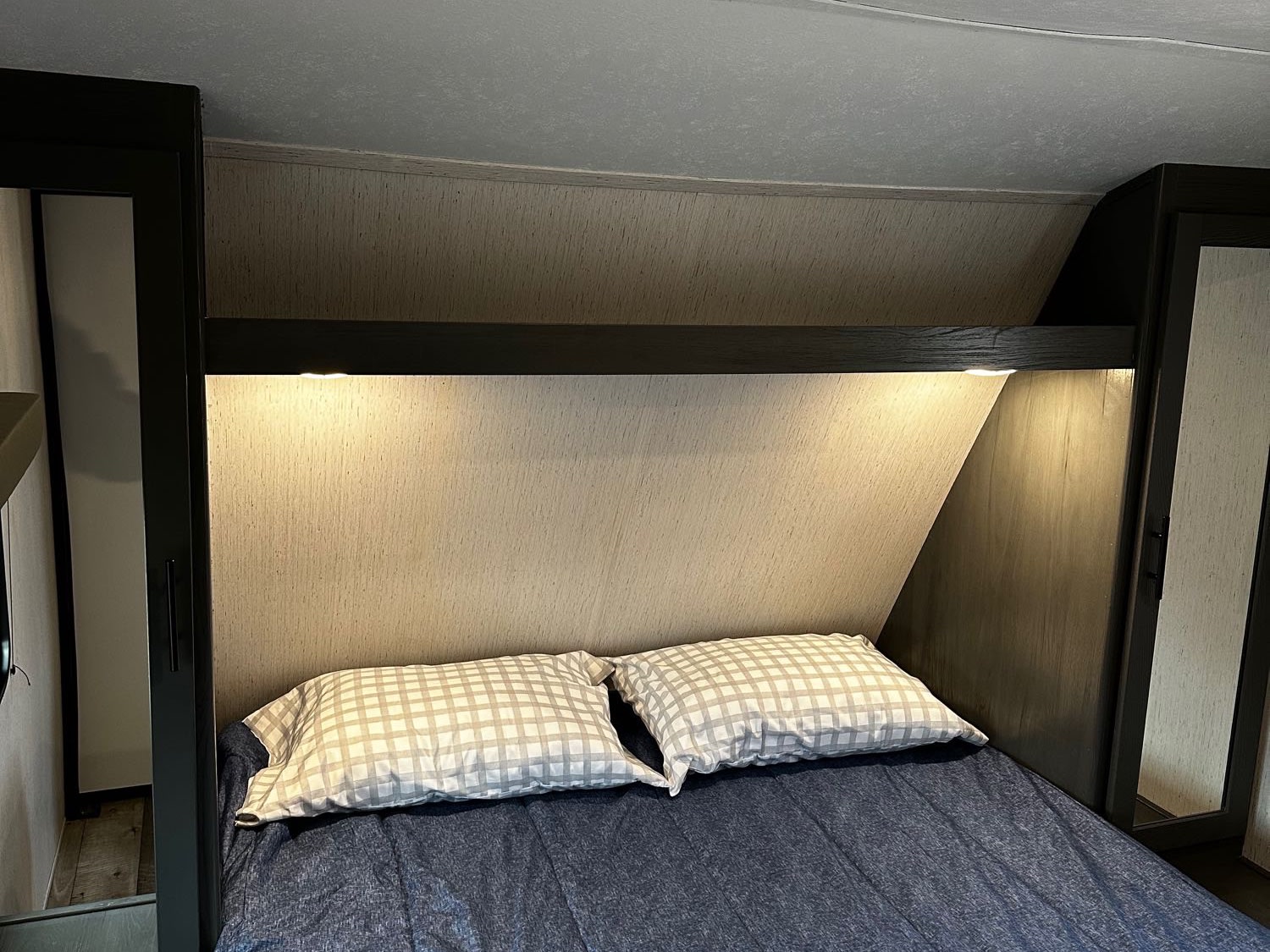 RV rental bedroom: a comfortable bed with blue bedding, plaid pillows, integrated lighting, and side cabinets for storage.. Aspen Trail Dutchmen 2022