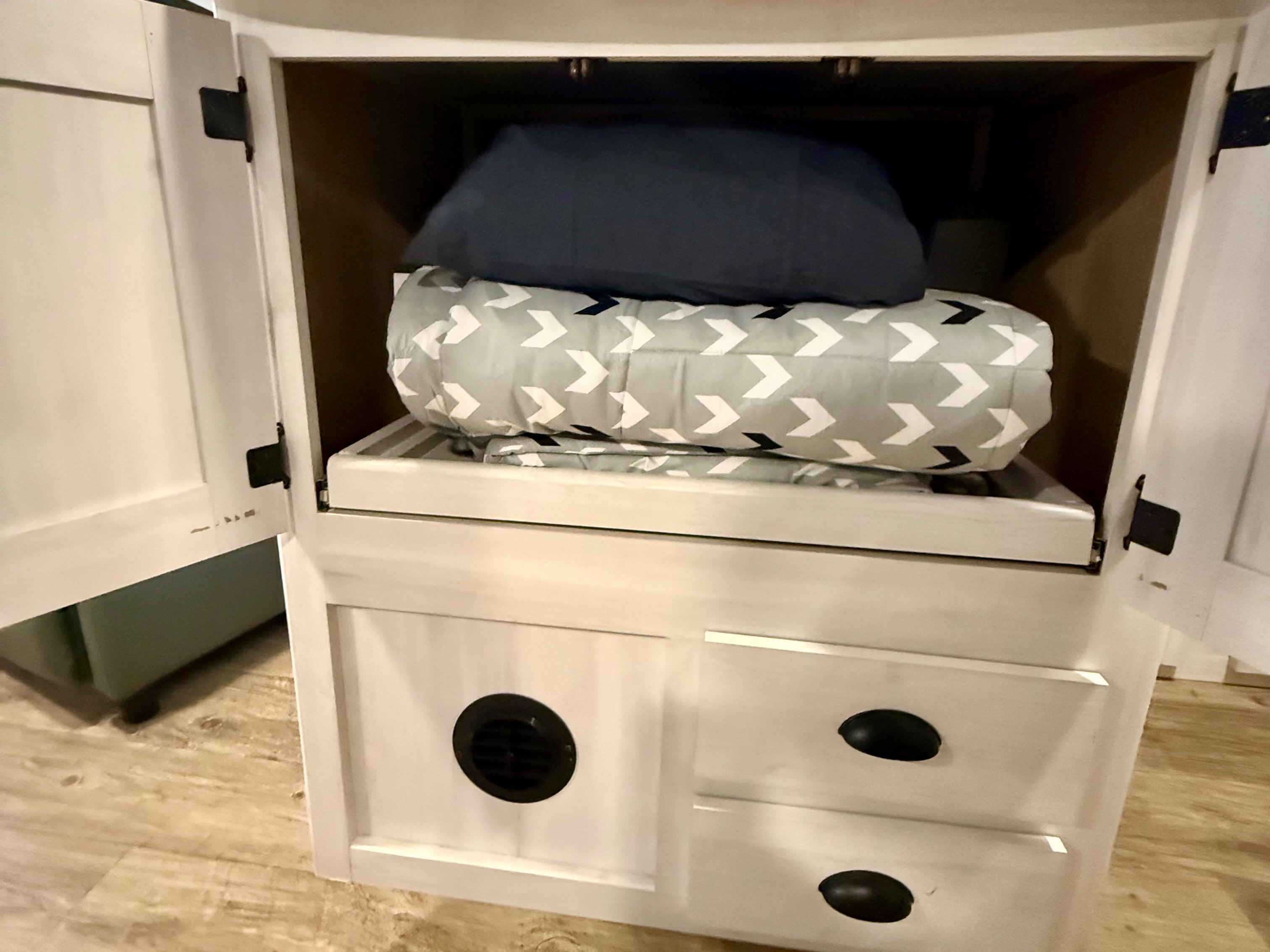 RV rental cabinet featuring neatly folded bedding, a convenient pull-out shelf, and lower storage drawers, optimizing small space organization.. Heartland RVs Trail Runner 2022