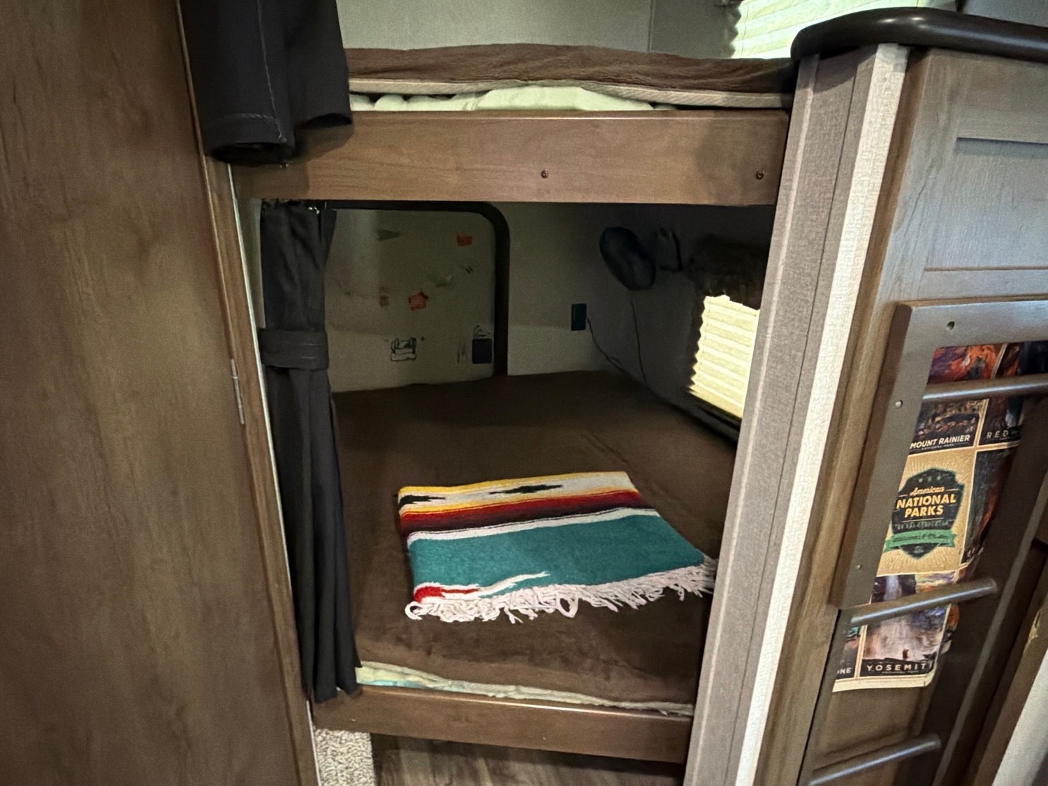 Cozy RV rental bunk beds with a colorful blanket, privacy curtain, and National Parks magazines. Perfect for camping!. Keystone RV Cougar 2019