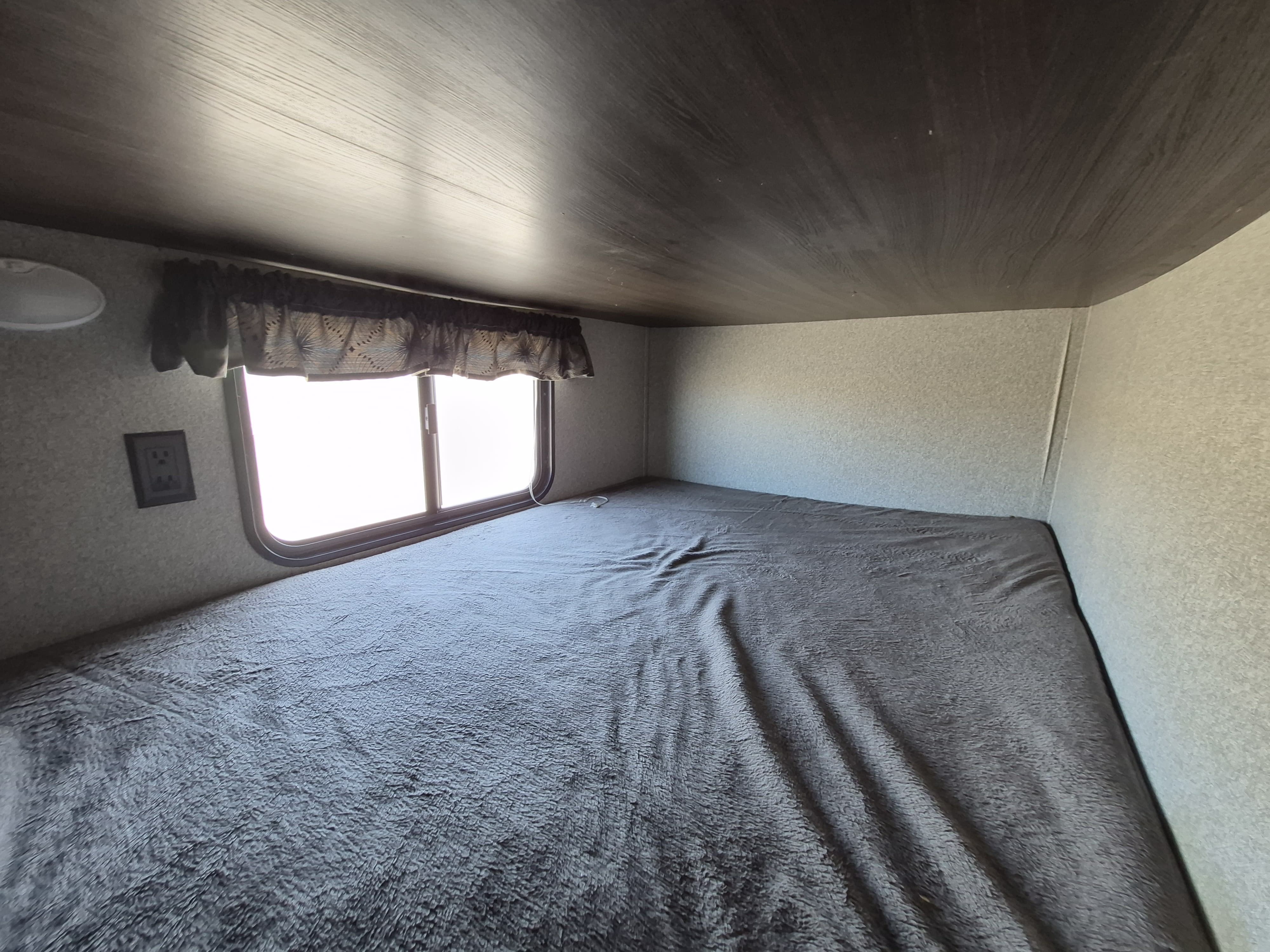 Cozy rv rental bunk bed with a window, dark blanket, and textured walls, offering a comfortable camper sleeping area.. Keystone RV Springdale 2019