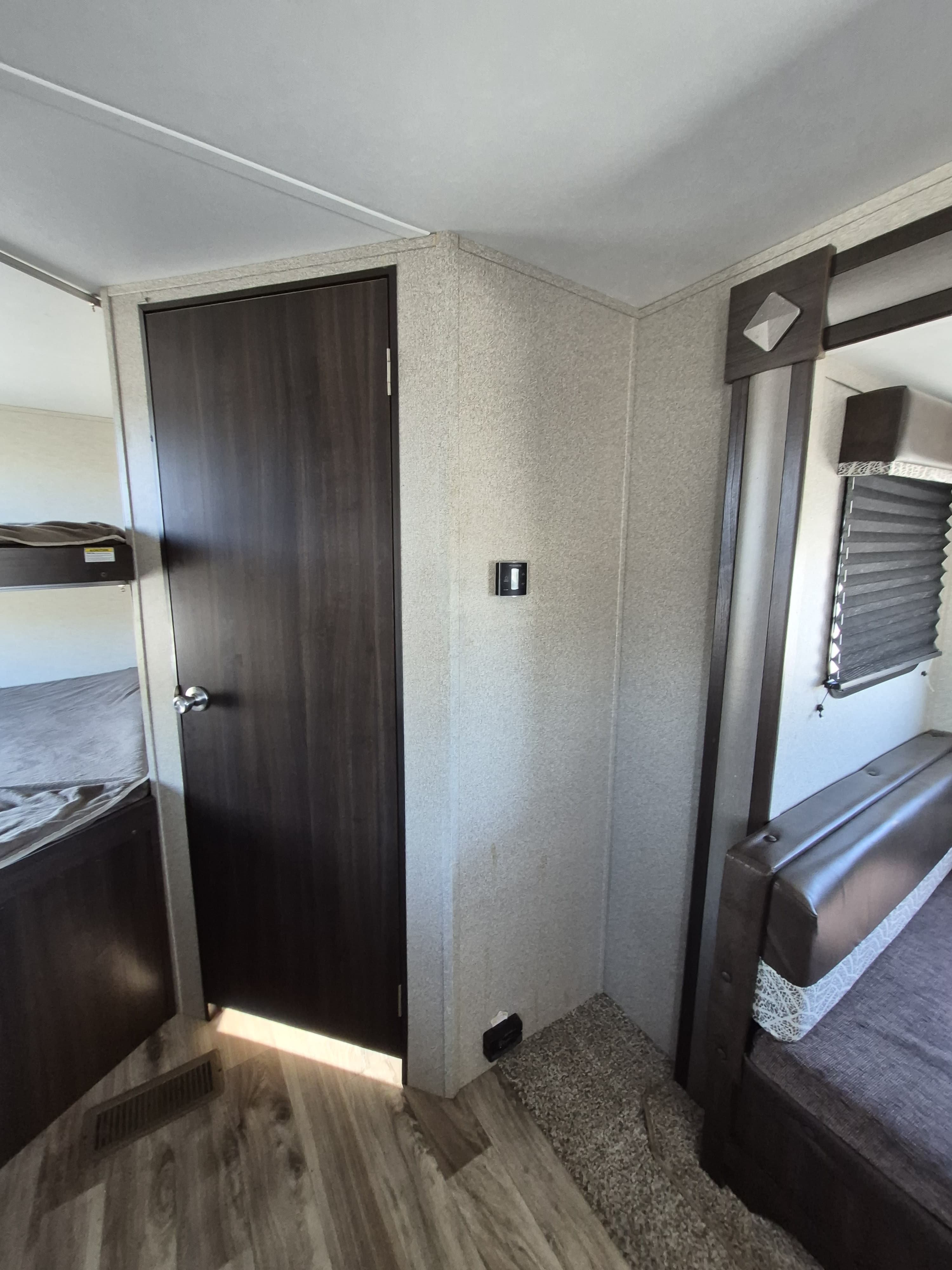 Interior of an RV rental: dark door, bunk beds left, dinette right with blinds, light textured walls, and mixed flooring.. Keystone RV Springdale 2019