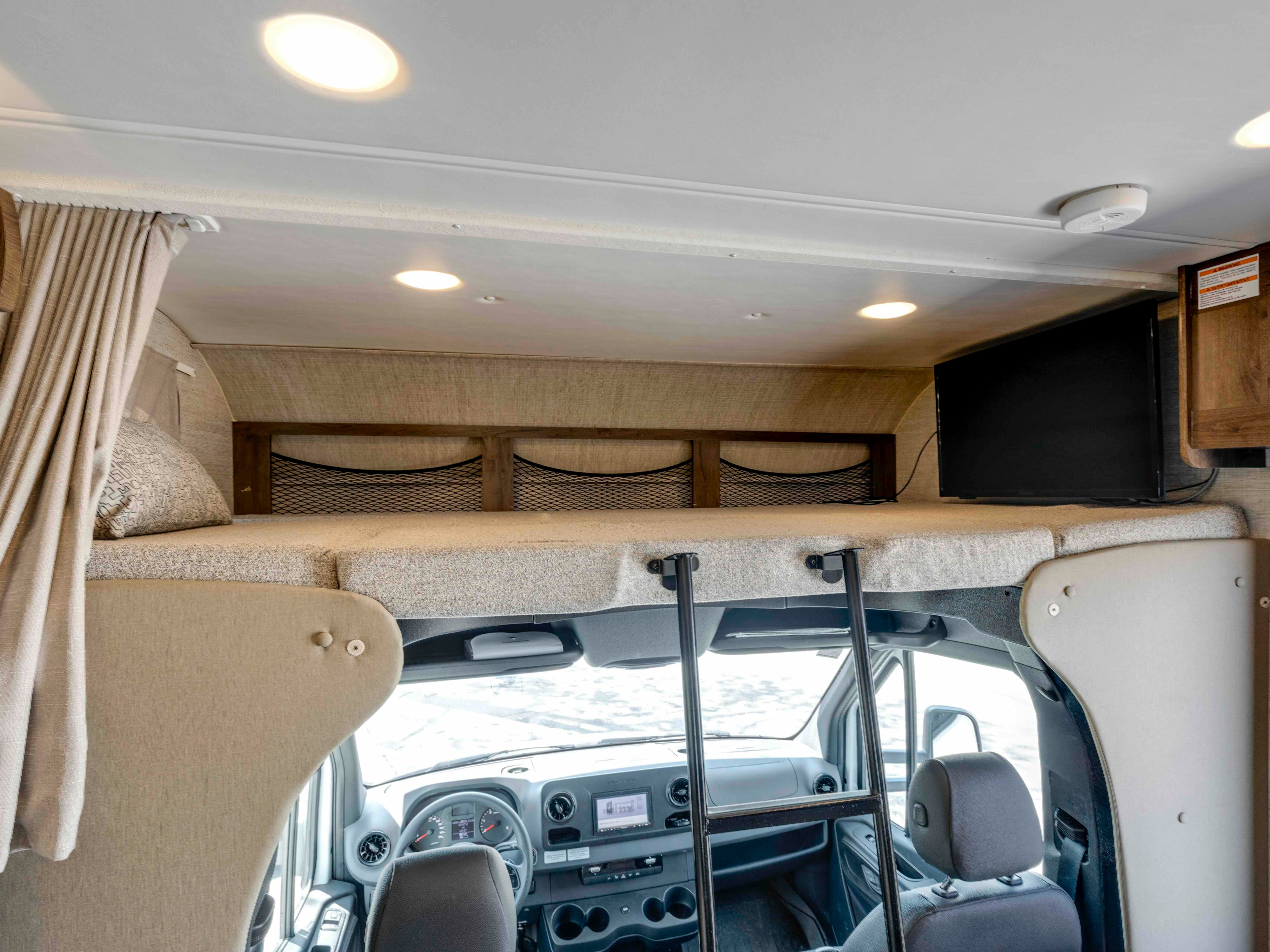 Inside this rv rental: an overhead sleeping area with a ladder, TV, and storage nets, positioned above the driver's cabin.. Jayco Melbourne 2022