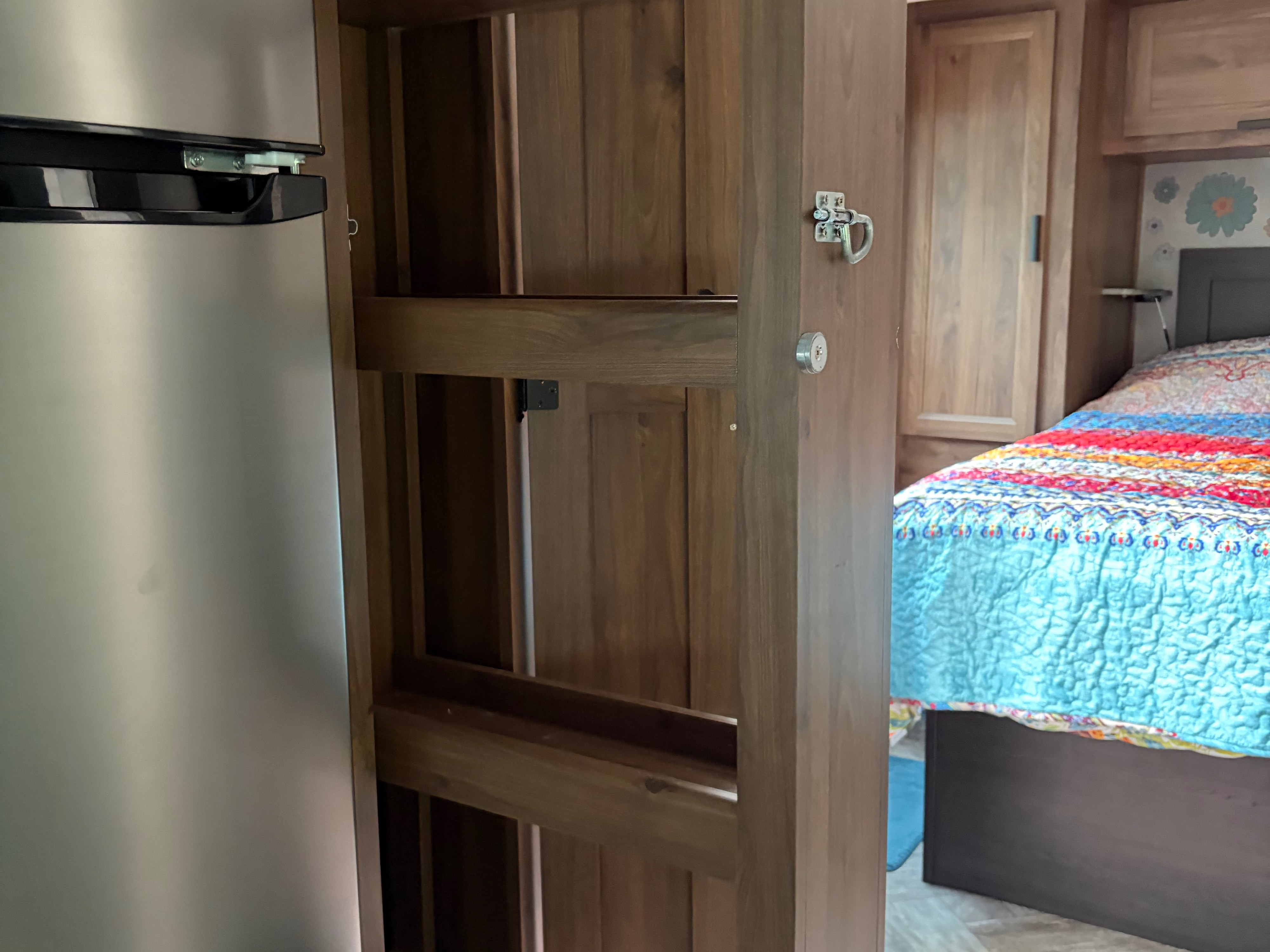 RV rental interior showing a stainless steel refrigerator, a wooden pantry with shelves, and a colorful bed in the bedroom.. Forester LE 2022