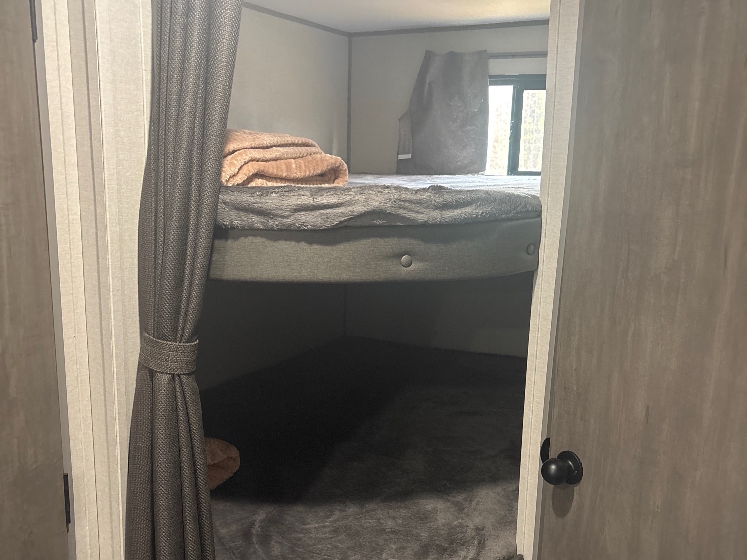 Cozy RV rental bunkhouse, featuring a top bunk with a blanket, a lower bunk, and a privacy curtain, with a window in the background.. Forest River Aurora Light 2025