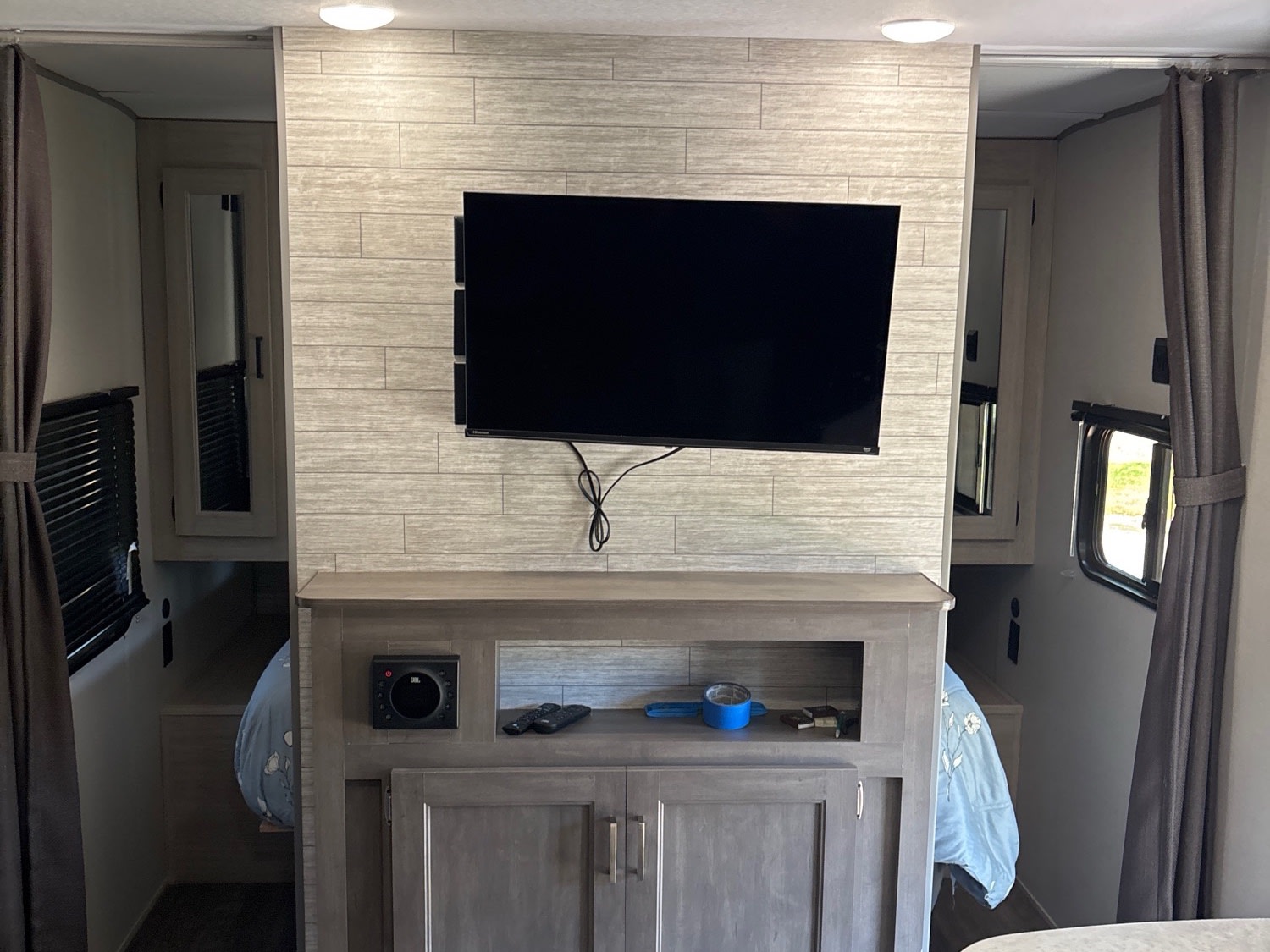 Inside this cozy RV rental: a central entertainment wall with TV, storage, and glimpses of the bedroom on both sides.. Forest River Aurora Light 2025