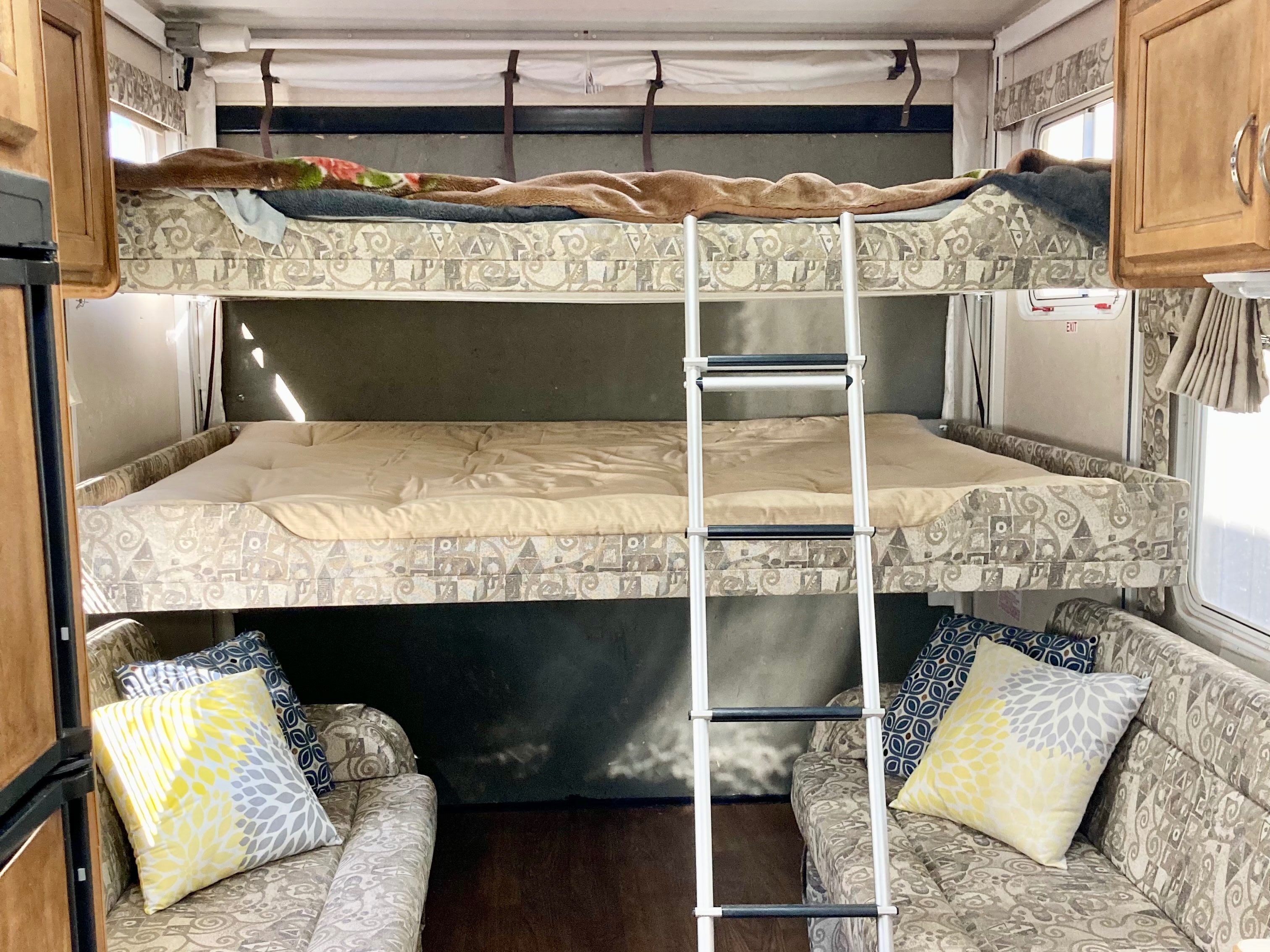 Spacious RV rental interior featuring comfortable bunk beds, a ladder, and twin seating areas with colorful pillows.. Rage'N Toy Hauler 2006