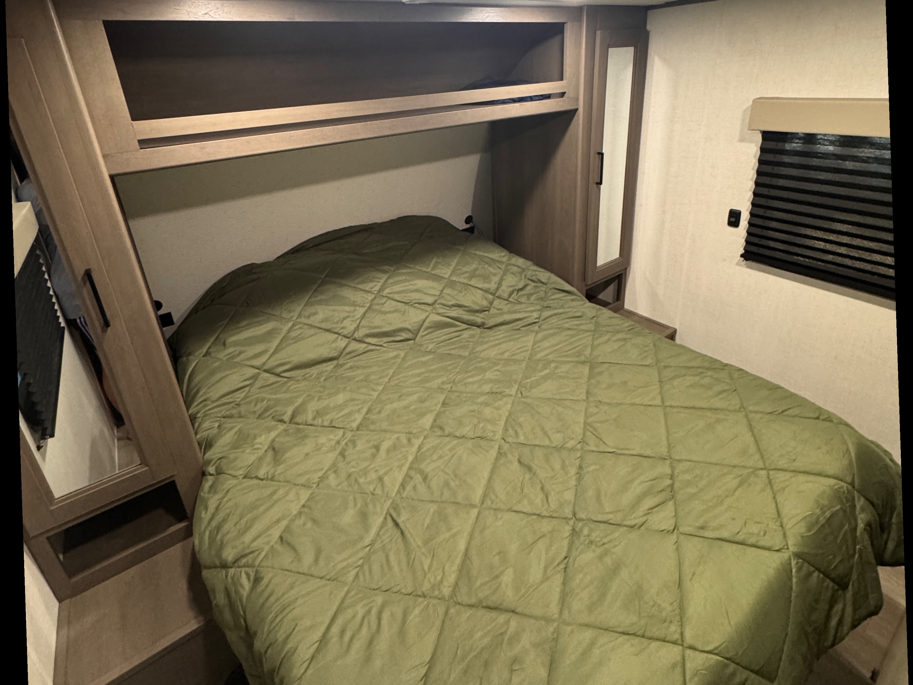 This RV rental's cozy bedroom features a green quilted bed, overhead shelf, and mirrored wardrobe.. Grand Design Transcend Xplor 2025